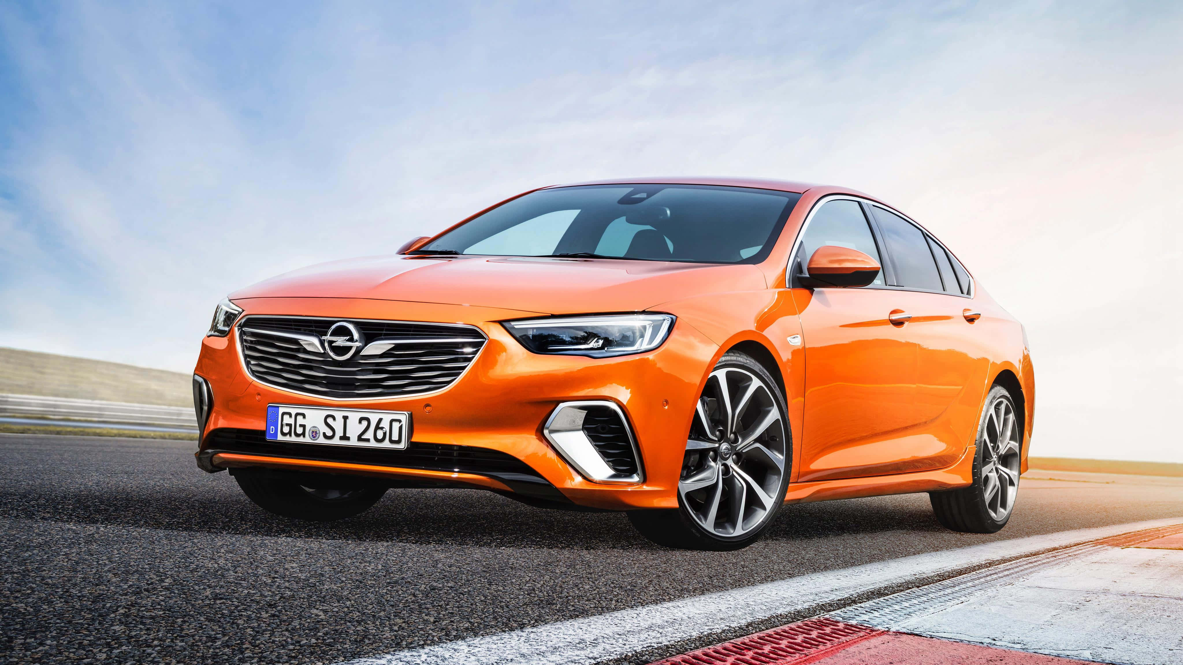 Opel Insignia 桌布 壁紙 — 一輛充滿活力的橙色歐寶房車在晴朗的藍天白雲下沿著賽道飛馳。