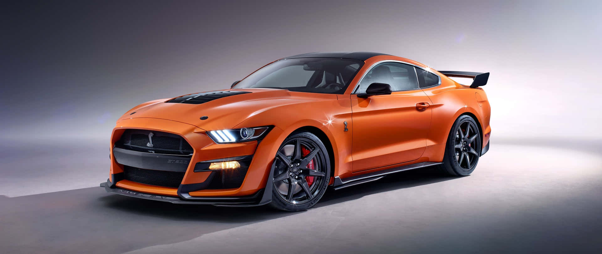  壁紙 — 一輛充滿活力的橙色福特野馬GT350R跑車，帶有黑色飾件和紅色制動卡鉗，在攝影棚內擺拍。