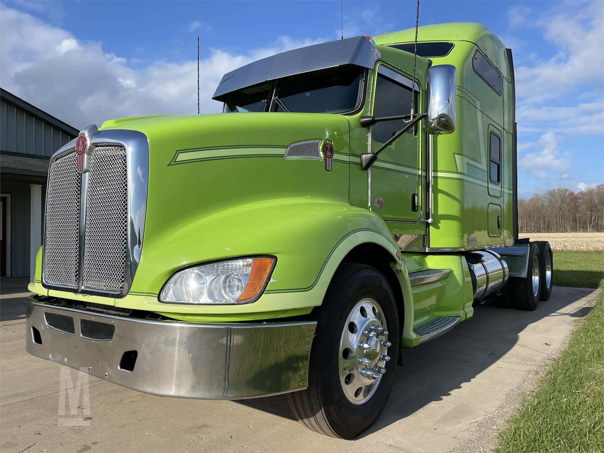 Kenworth T660 桌布 壁紙 — 一輛充滿活力的青檸綠色半掛卡車，帶有鍍鉻裝飾，停在混凝土墊上，旁邊是草地，天空部分多雲。