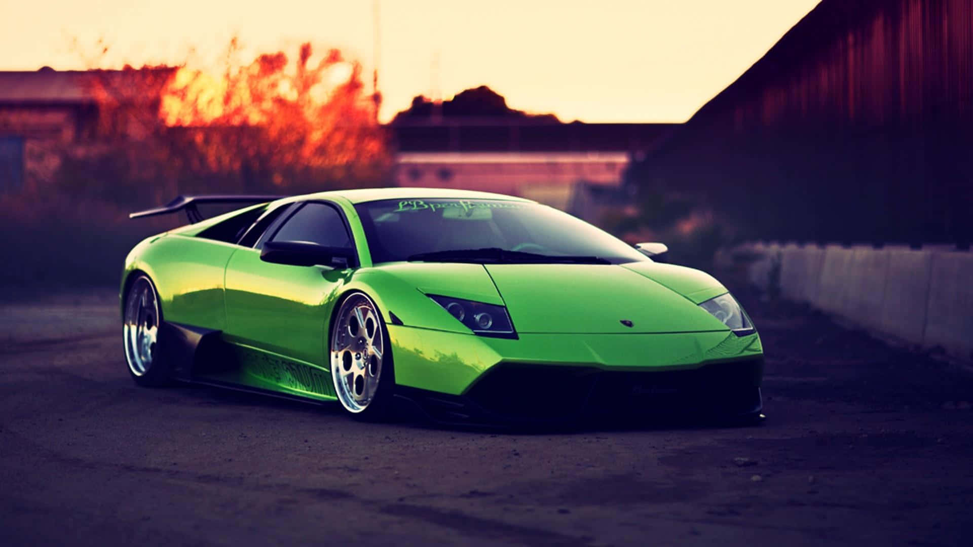 Lamborghini Murciélago 桌布 壁紙 — 一輛充滿活力的綠色林寶堅尼 Murciélago 在熾熱的夕陽下閃閃發光，在粗糙的城市街道上投下長長的影子。