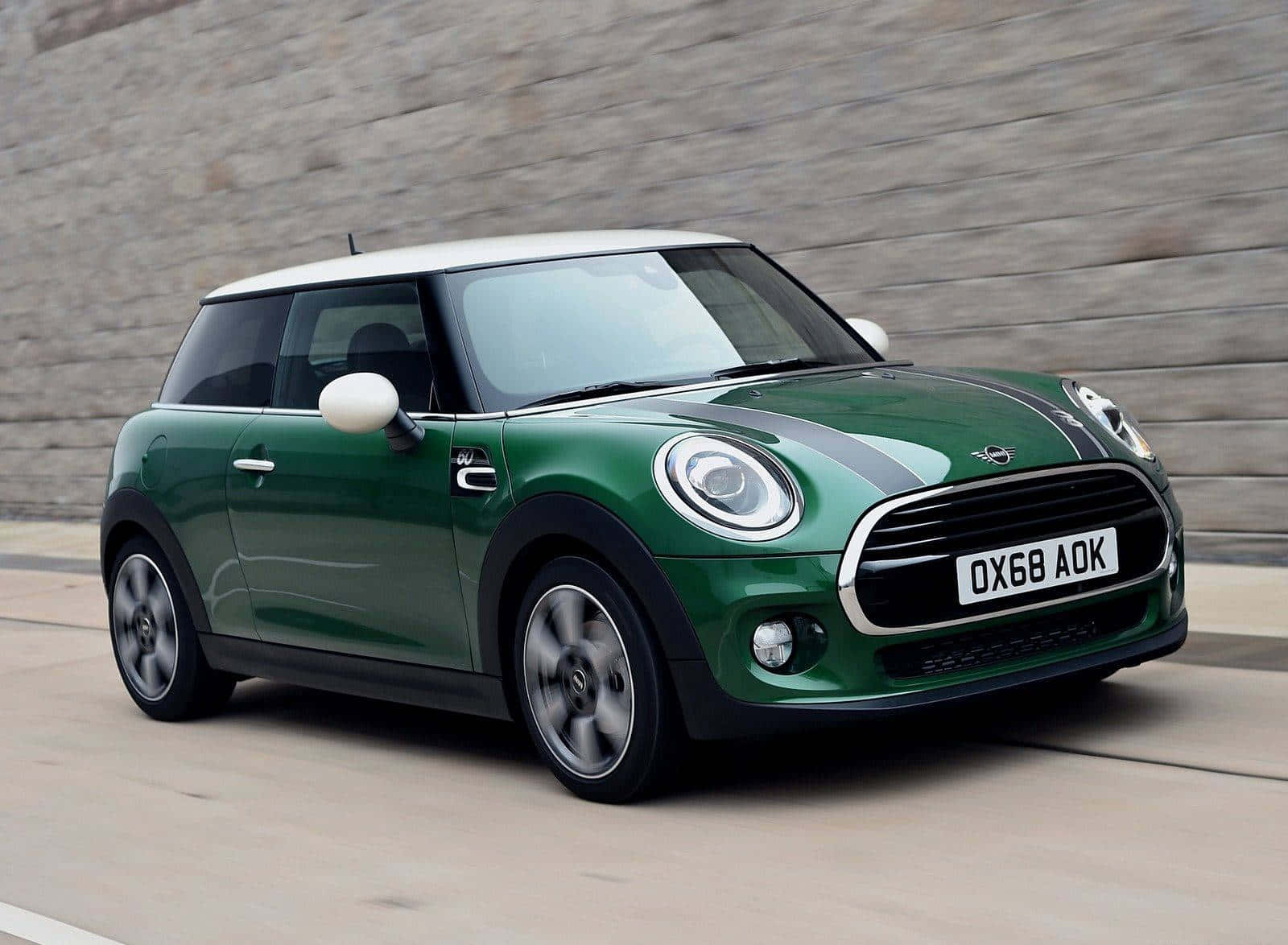 壁紙 — 一輛充滿活力的綠色Mini Cooper，白色車頂，沿著石牆旁的道路飛馳。
