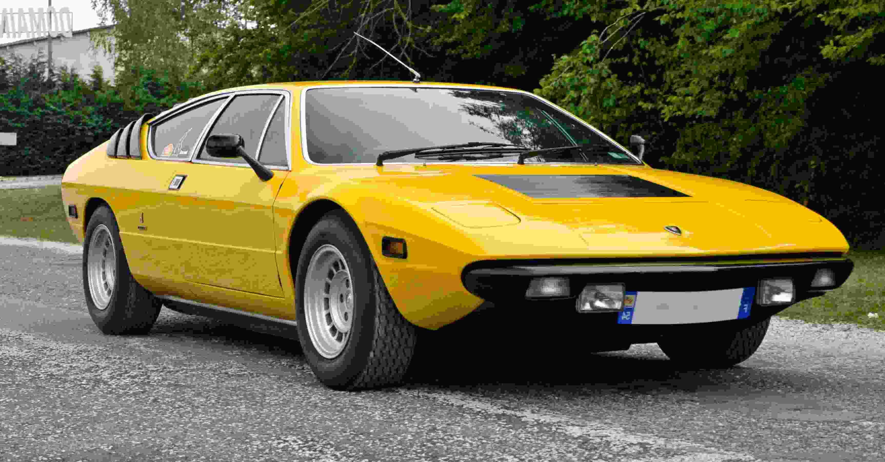 Lamborghini Urraco 桌布 壁紙 — 一輛充滿活力的黃色經典跑車停泊在碎石車道上，周圍環繞著茂密的綠樹。