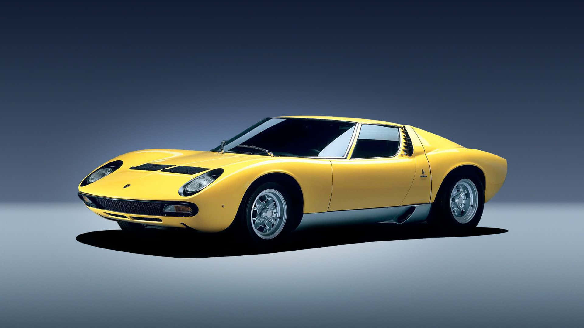 Lamborghini Miura 桌布 壁紙 — 一輛充滿活力的黃色林寶堅尼Miura跑車，帶有黑色賽車條紋，在漸變灰色工作室背景前蓄勢待發。
