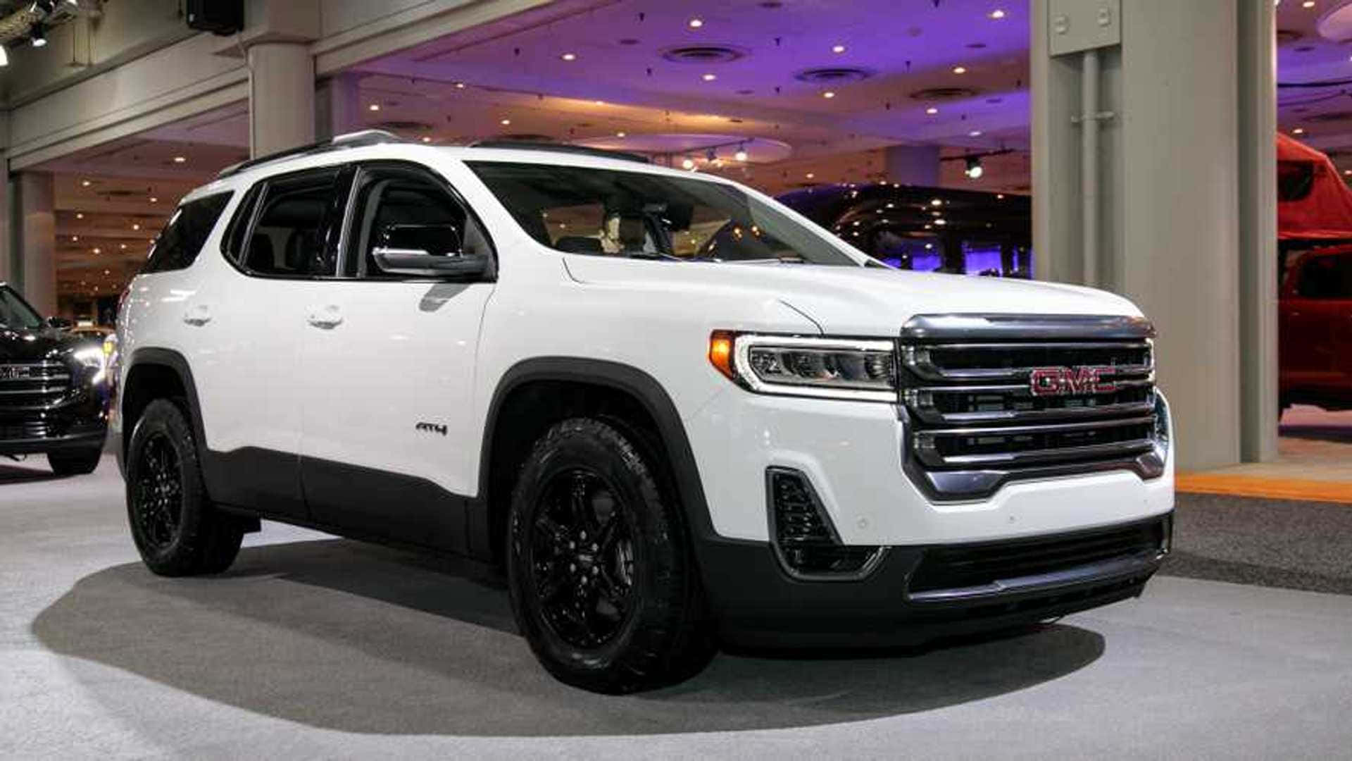 Gmc Acadia 桌布 壁紙 — 一輛帶有黑色飾邊和輪圈的純白色GMC Acadia SUV在寬敞的室內汽車展廳中，在明亮的展覽燈光下展示。