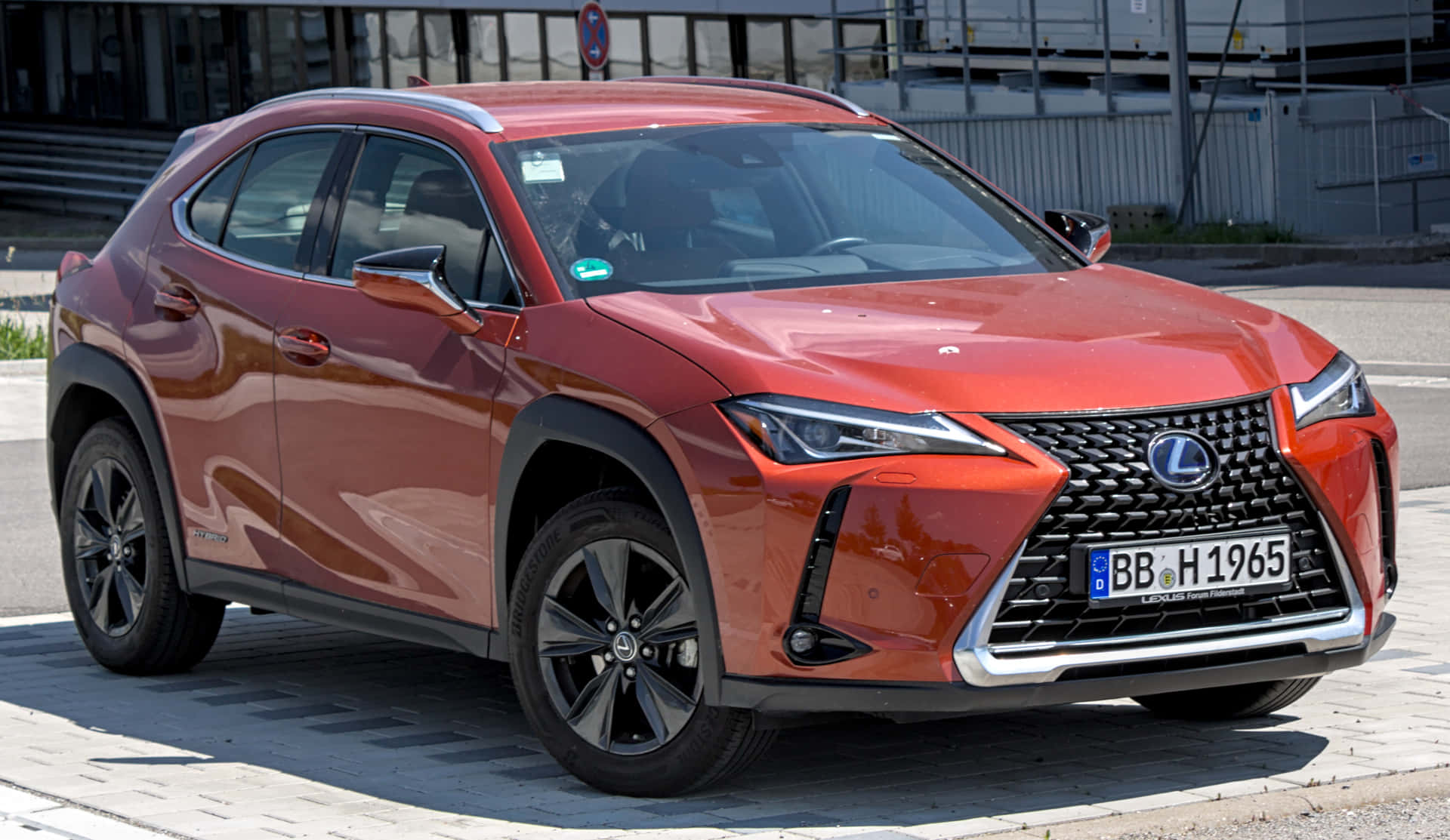  壁紙 — 一輛光澤的紅色Lexus UX SUV在明亮的日光下停泊在鋪砌的城市街道上。
