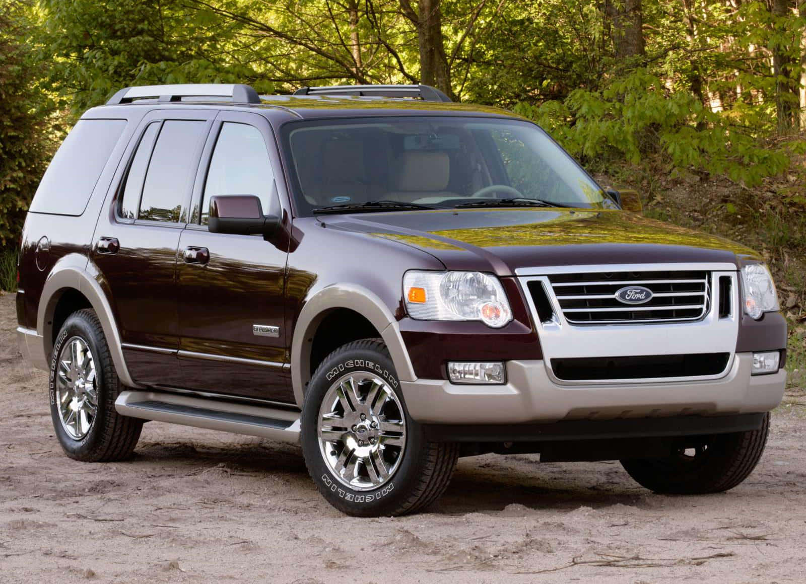 Ford Explorer 桌布 壁紙 — 一輛酒紅色福特探險者SUV，帶有鍍鉻裝飾，停在由茂密綠樹環繞的泥路上。