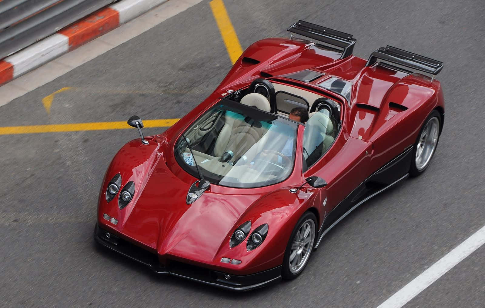Pagani Zonda C12 Roadster 桌布 壁紙 — 一輛亮紅色的帕加尼Zonda跑車在黃白相間的賽道邊緣下，於明亮的日光中疾馳。