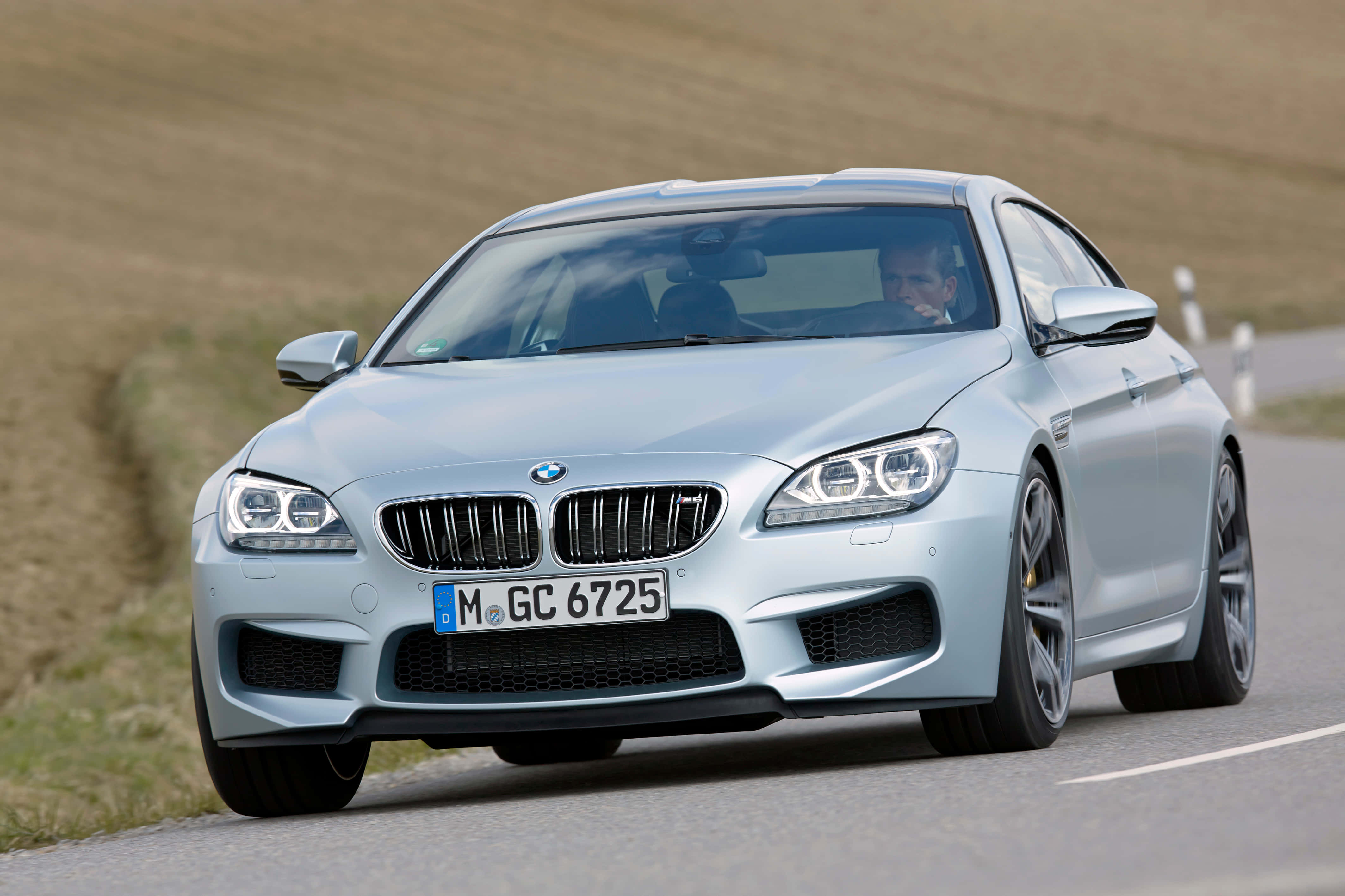Bmw M6 桌布 壁紙 — 一輛銀色寶馬M6雙門跑車在蜿蜒的鄉村道路上飛馳，司機透過擋風玻璃可見。