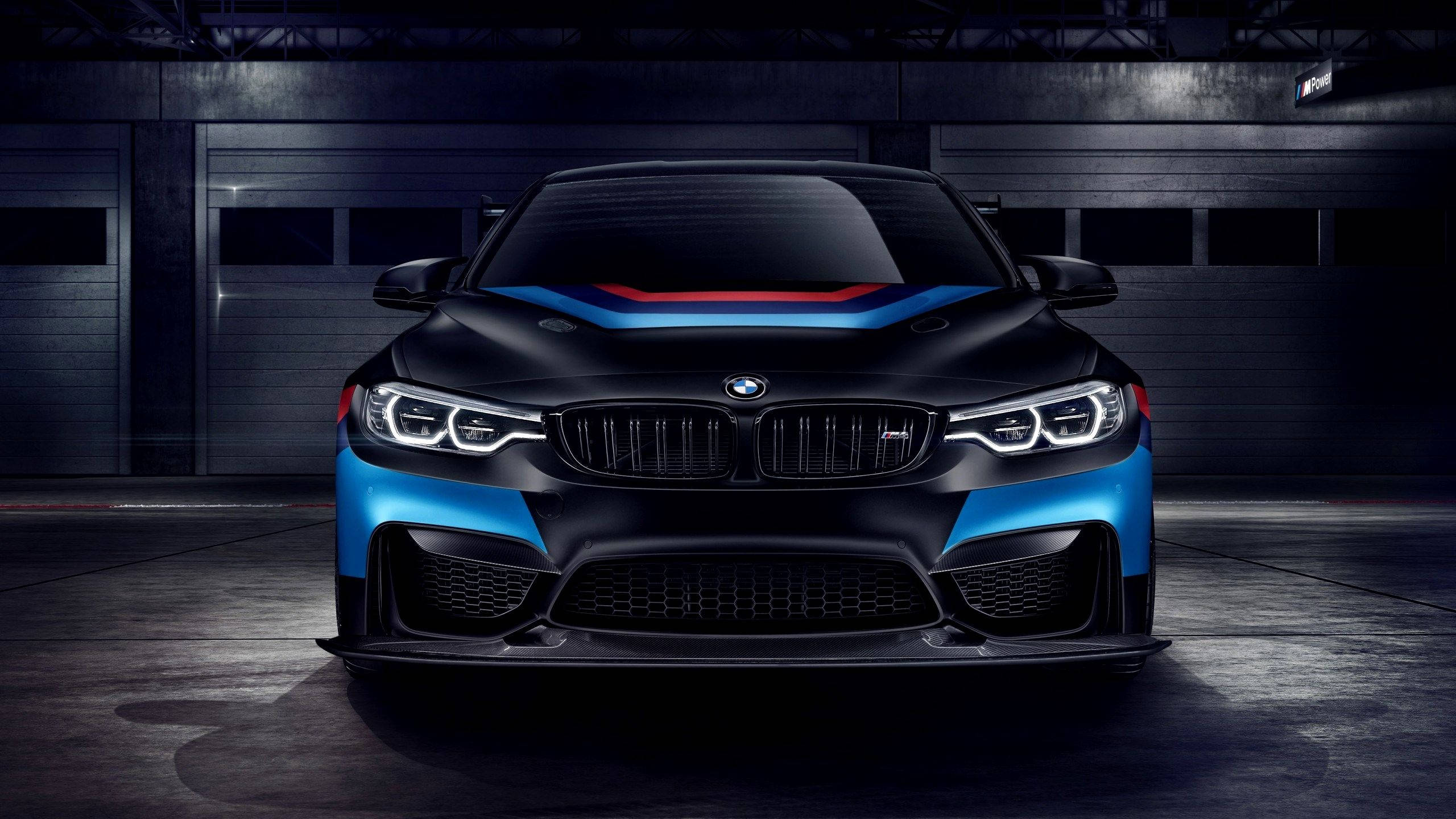 黑色BMW M2，帶有藍色和紅色條紋，停在昏暗的車庫中。