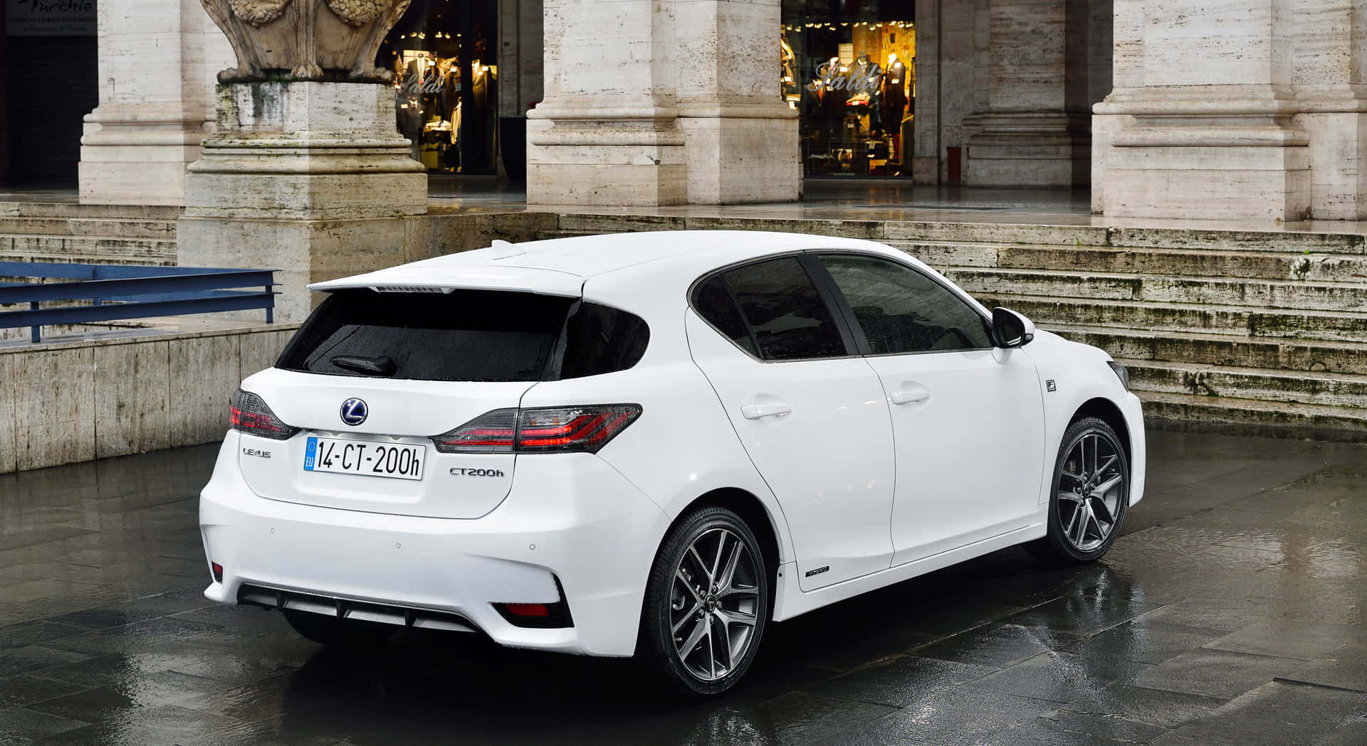 Lexus Ct 200h 桌布 壁紙 — 一輛時尚的白色Lexus CT200h混合動力掀背車停在濕滑路面上，位於石柱下方，背後商店櫥窗閃爍著光芒。