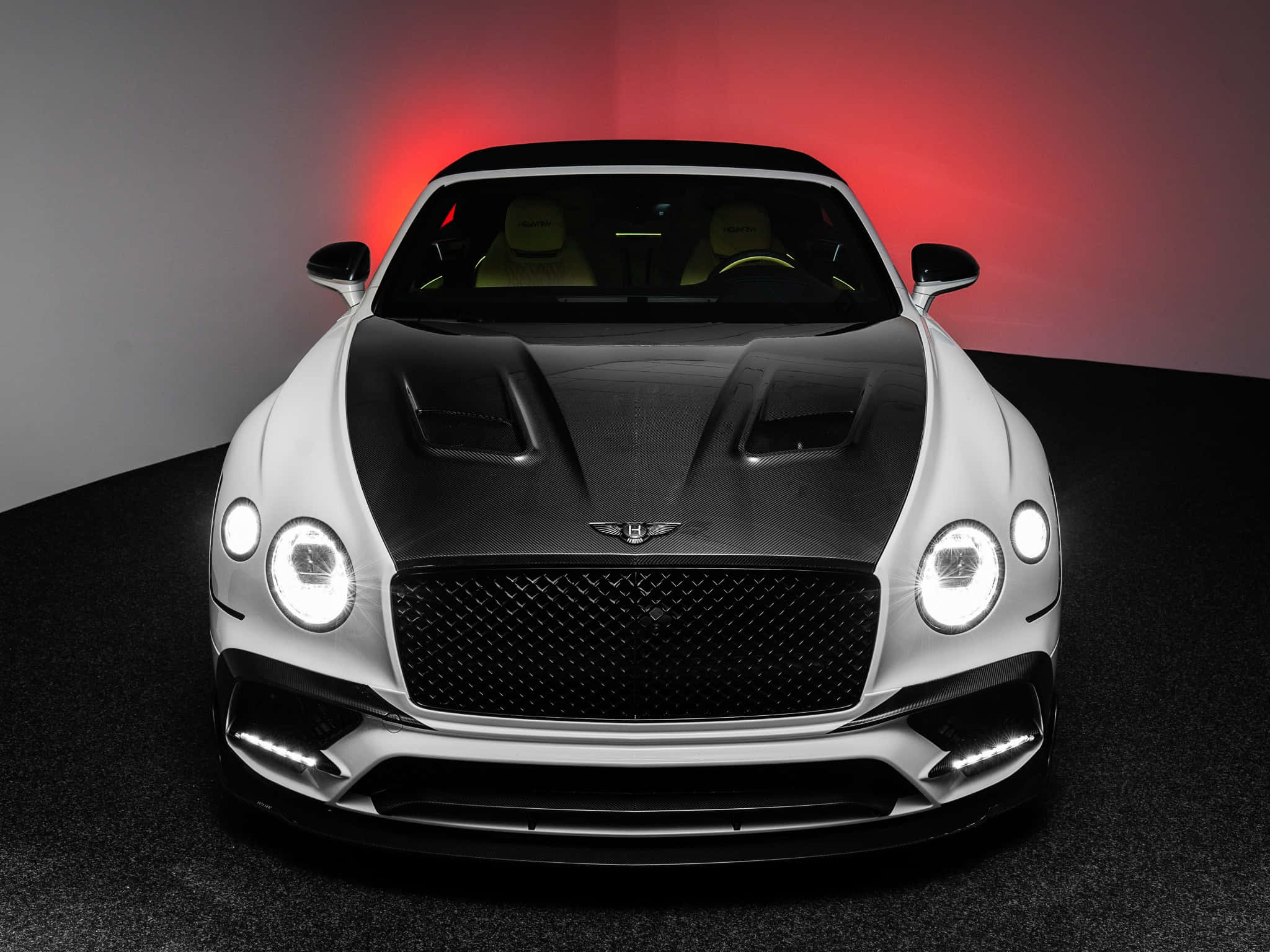 Bentley Continental Gt 桌布 壁紙 — 一輛時尚的白色賓利，帶有黑色碳纖維引擎蓋和發光車頭燈，在戲劇性的紅色工作室燈光下居中。