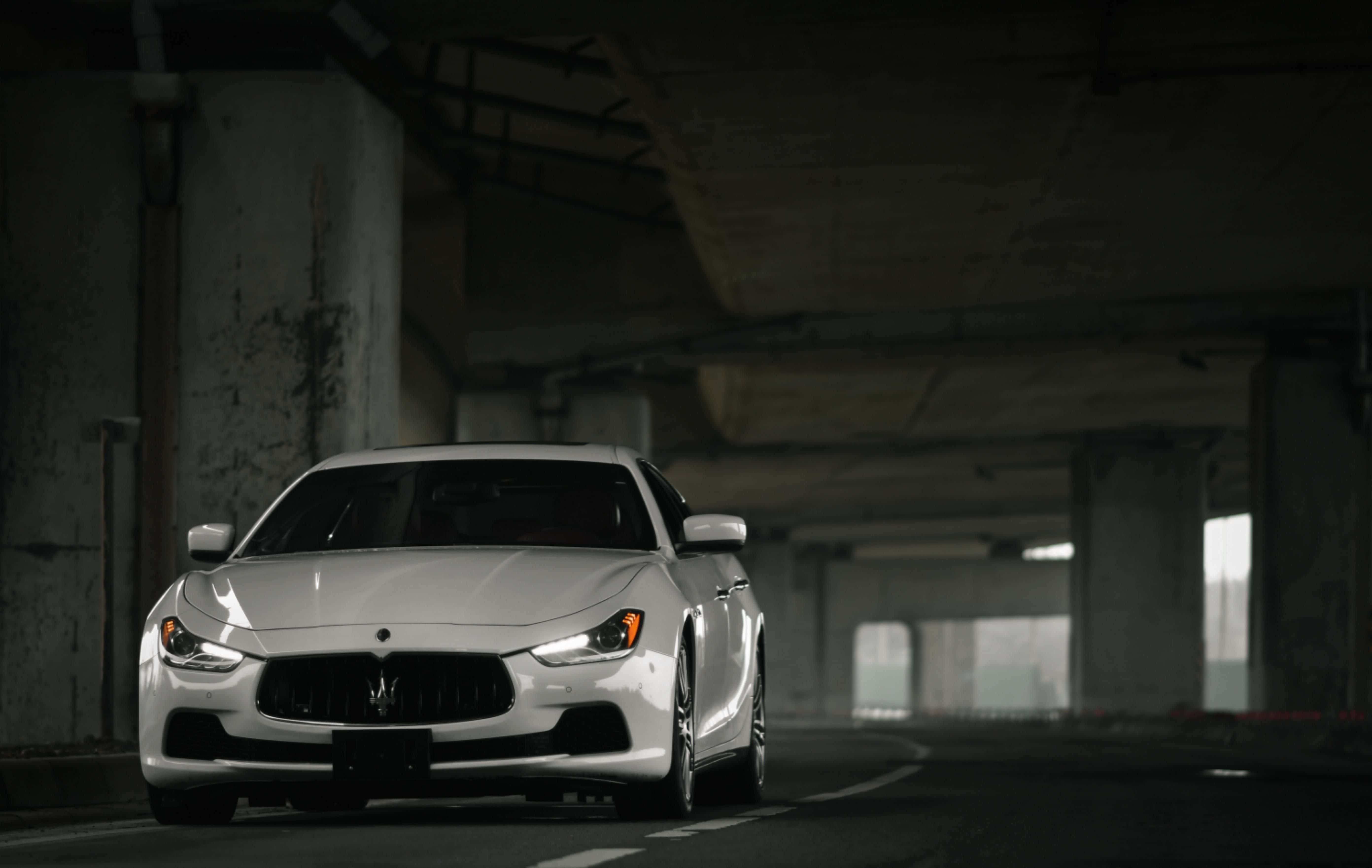 Maserati Ghibli 桌布 壁紙 — 一輛時尚的白色瑪莎拉蒂跑車在燈光昏暗的混凝土天橋下滑行，帶有戲劇性的燈光效果。