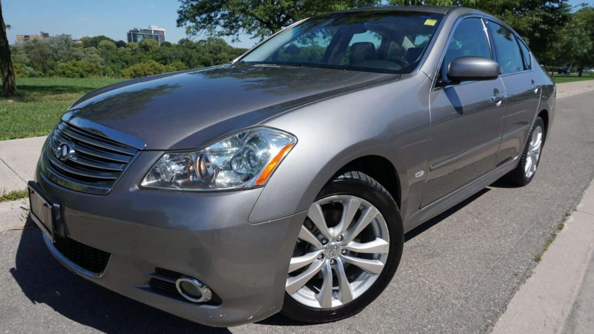 Infiniti M35 桌布 壁紙 — 一輛時尚的銀色Infiniti房車停泊在陽光明媚的街道上，背景有綠樹和建築物。