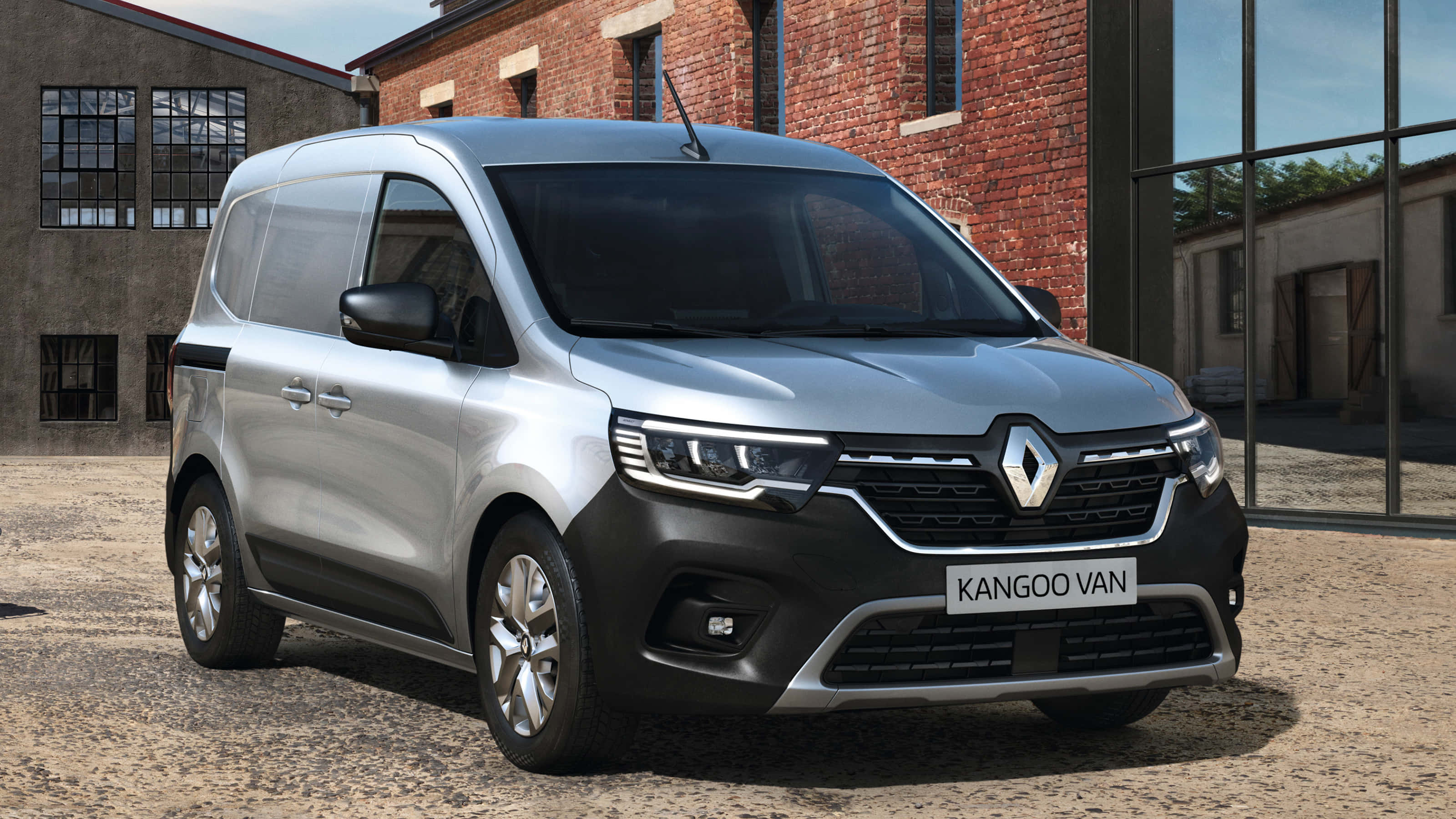 Renault Kangoo 桌布 壁紙 — 一輛時尚的銀色雷諾Kangoo客貨車停泊在紅磚工業大樓前的礫石上，大樓有大型玻璃窗。