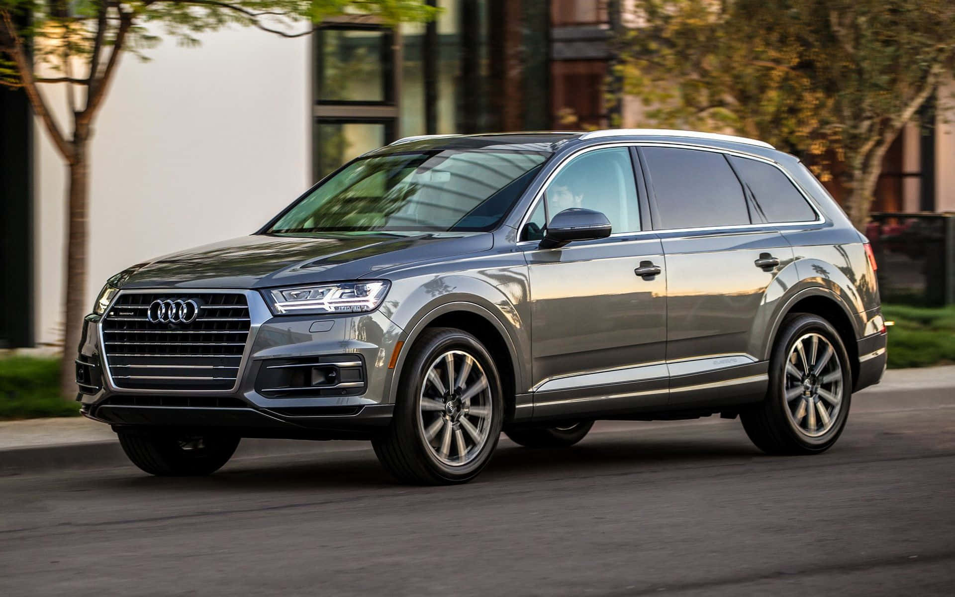 Audi Q7 桌布 壁紙 — 一輛時尚的銀色Audi Q7 SUV停泊在城市的街道上，背景是現代建築和樹木。