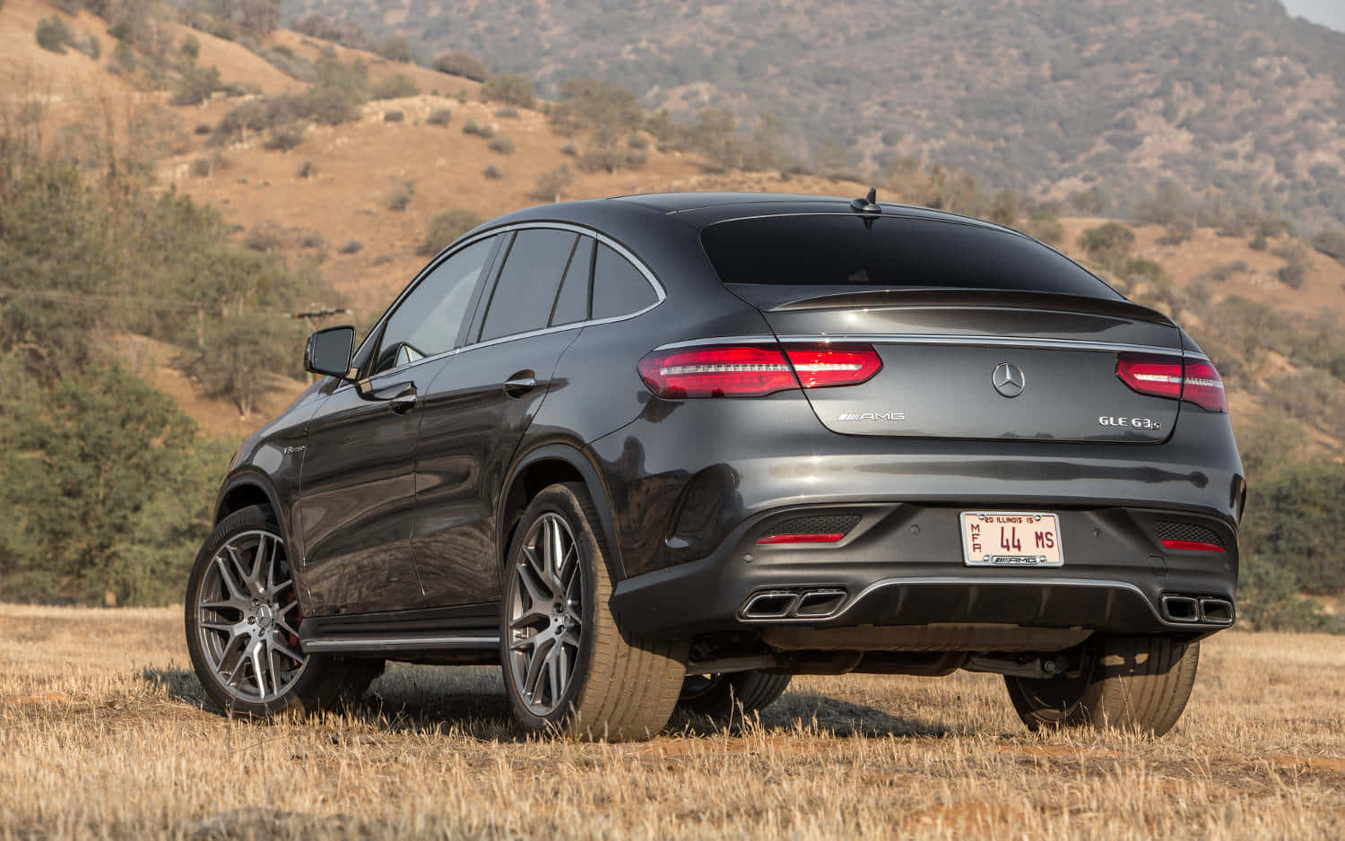 Mercedes Benz Gle-class 桌布 壁紙 — 一輛時尚的深灰色 Mercedes-AMG GLC 63 S Coupe 停在乾草上，背景是起伏的丘陵。