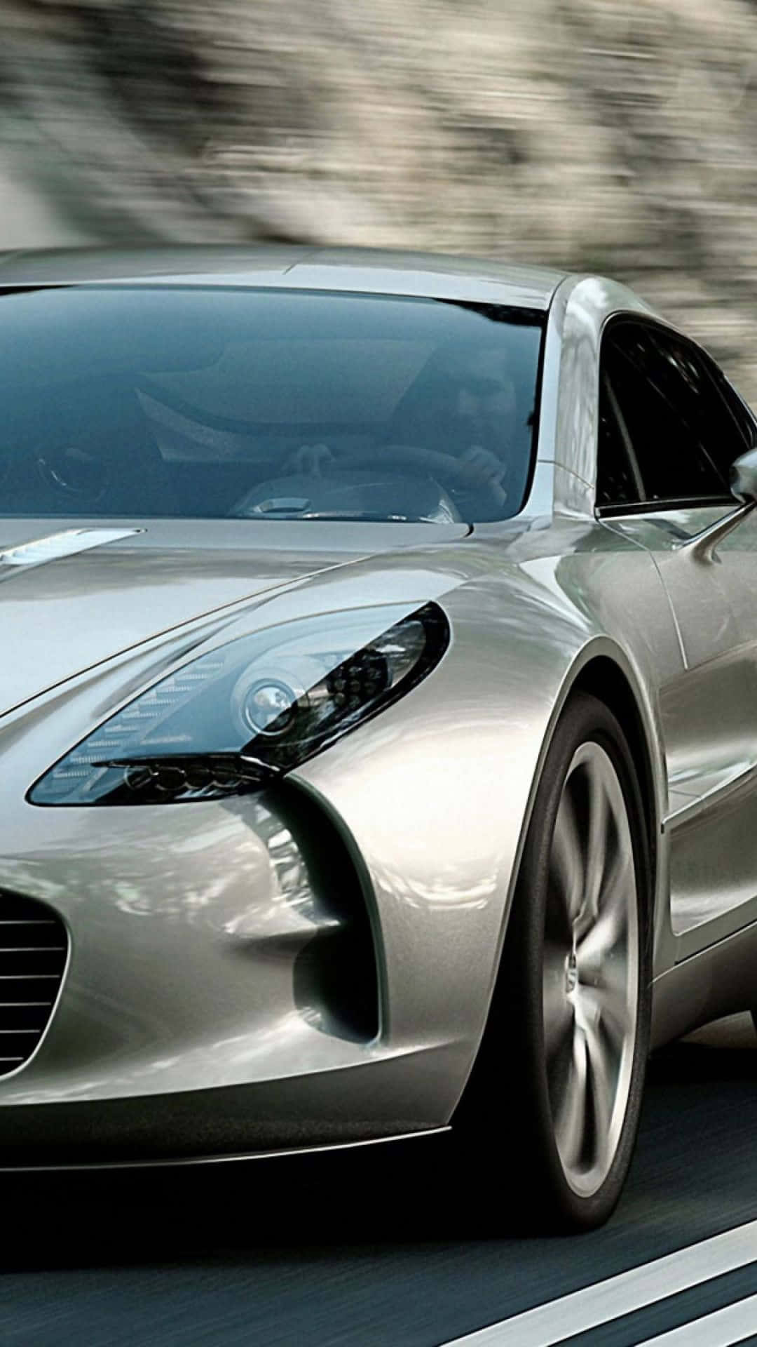 Aston Martin One-77 桌布 壁紙 — 一輛時尚的銀色跑車在道路上疾馳，背景呈現動態模糊效果。