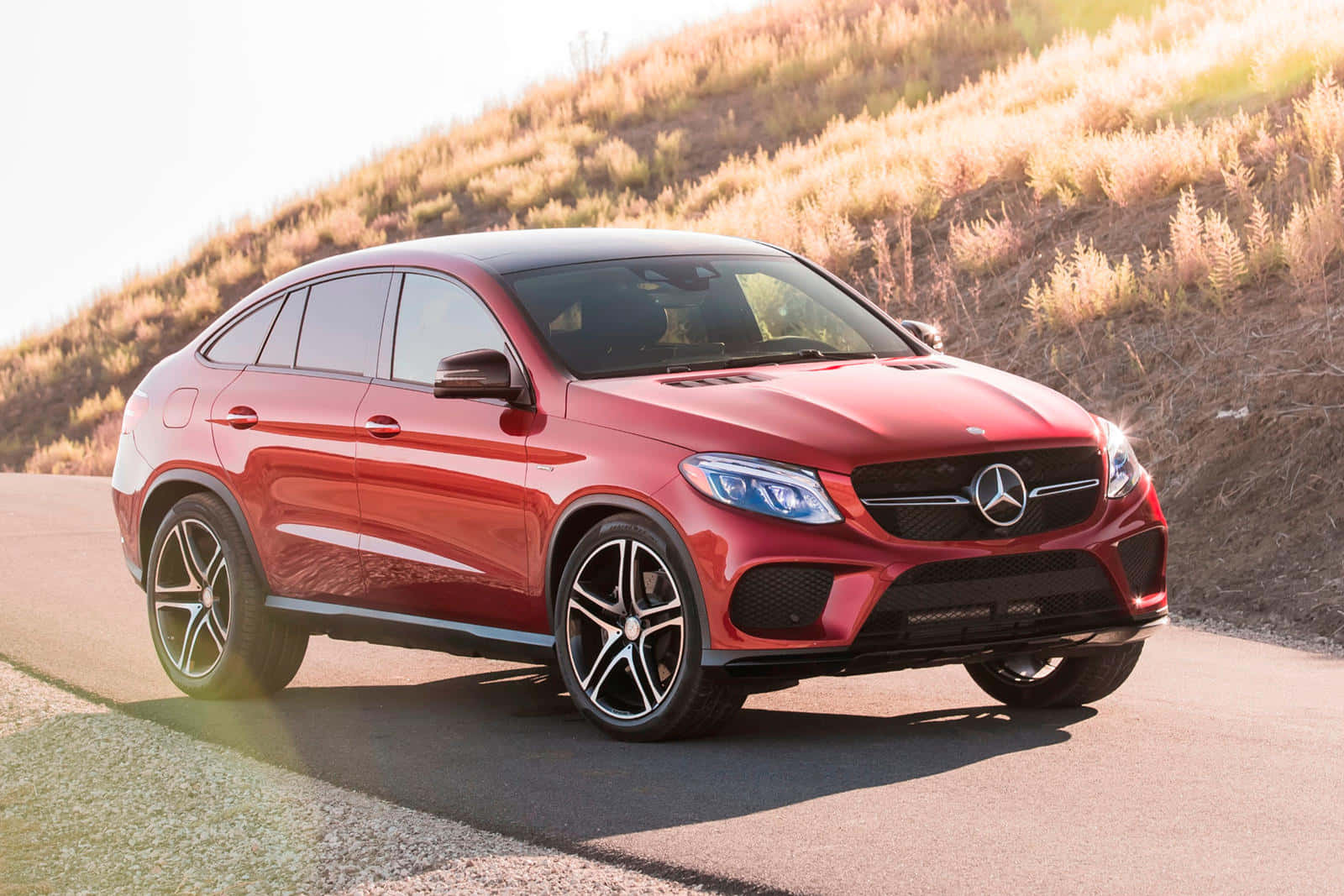 Mercedes Benz Gle-class 桌布 壁紙 — 一輛閃亮的紅色Mercedes-AMG GLE Coupe在陽光明媚的山路上行駛，背景是金色的草坡。