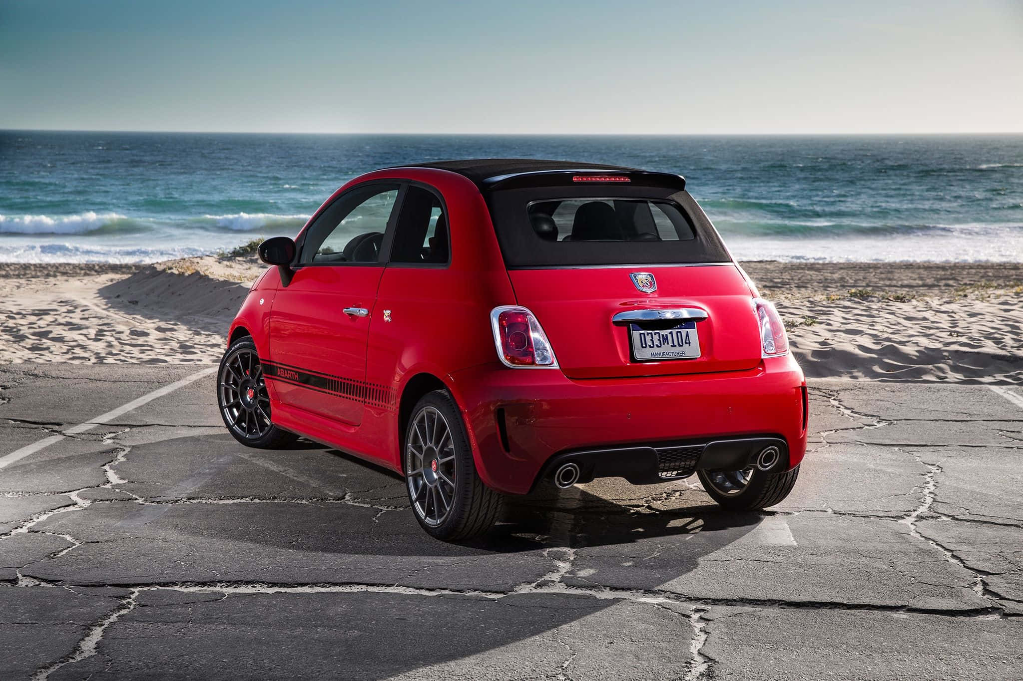 Fiat 500l 桌布 壁紙 — 一輛鮮紅色的菲亞特500停在裂開的人行道上，旁邊是沙灘，海浪在清澈的藍天下拍打。