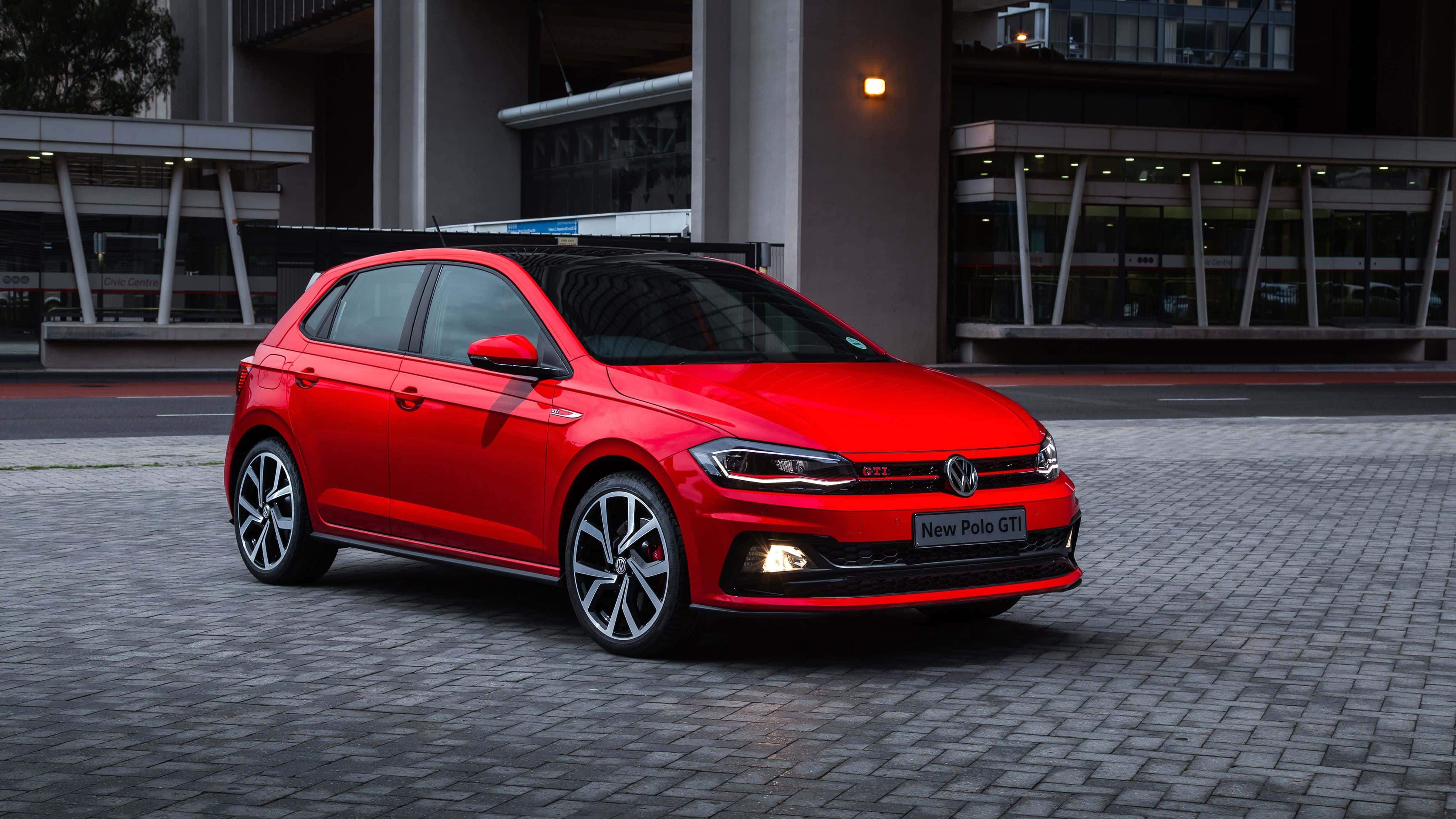 Volkswagen Polo 桌布 壁紙 — 一輛鮮紅色的福士Polo GTI停泊在鋪砌的都市廣場上，背景是現代建築。