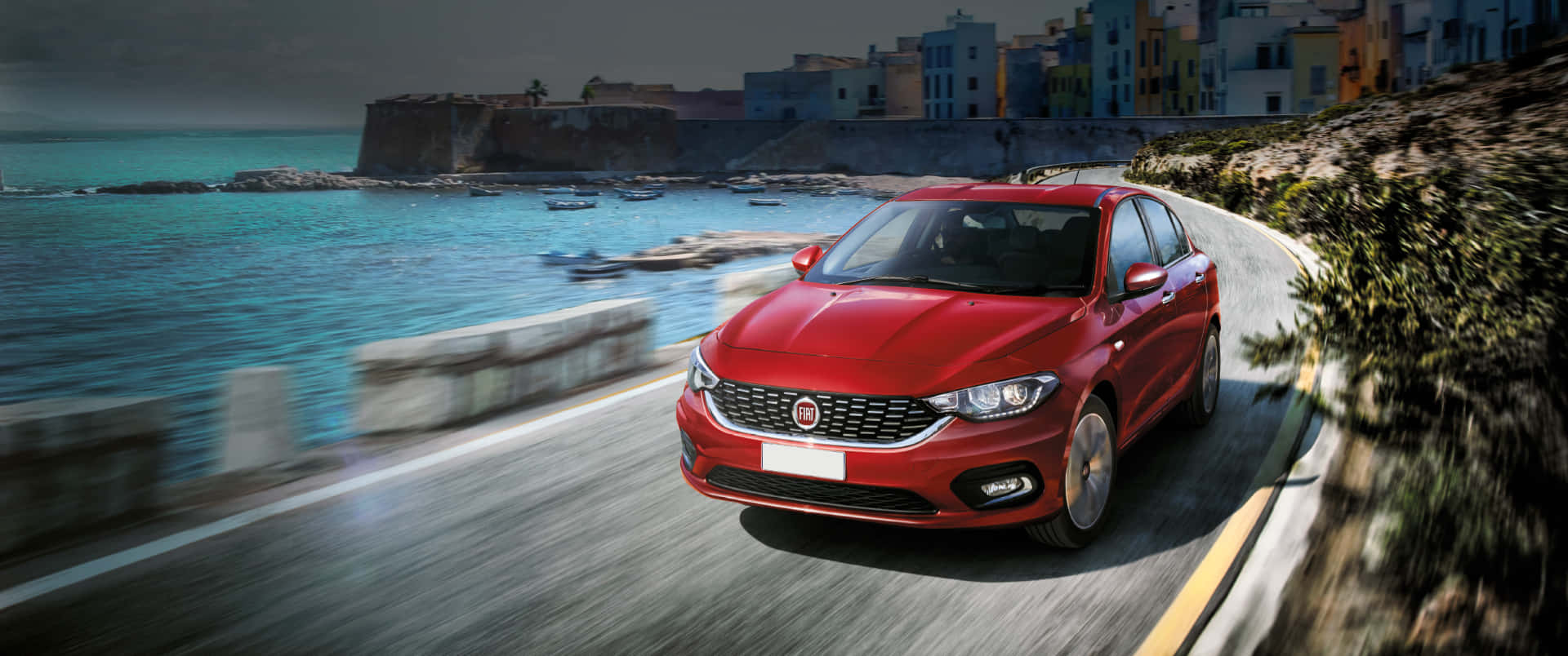 Fiat Tipo 桌布 壁紙 — 一輛鮮紅色的轎車沿著海岸公路飛馳，背景是碧綠的海水和色彩繽紛的懸崖建築。