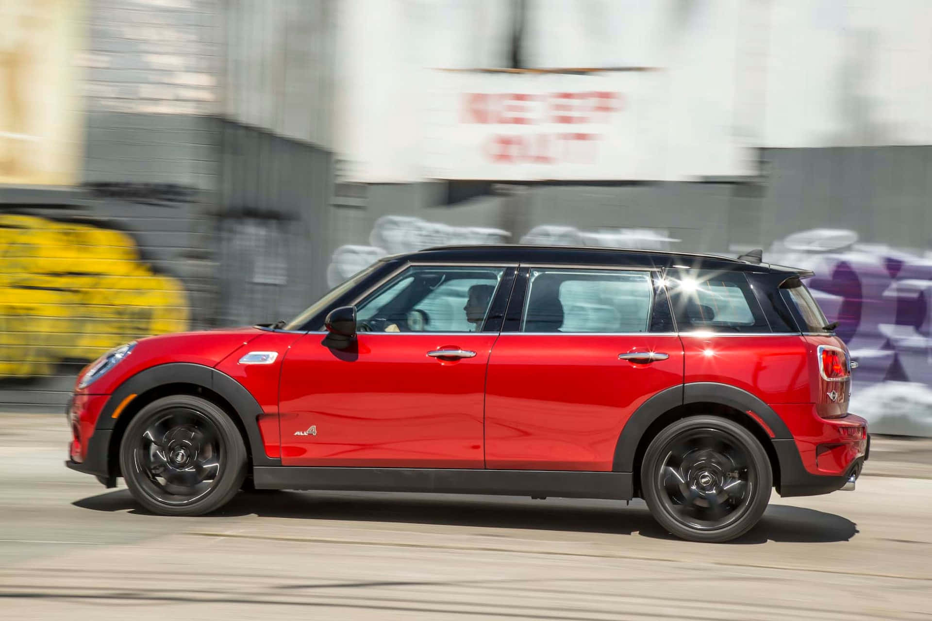 Mini Cooper S Clubman All4 桌布 壁紙 — 一輛鮮紅色的MINI Countryman在明亮的日光下高速駛過模糊的城市牆壁。