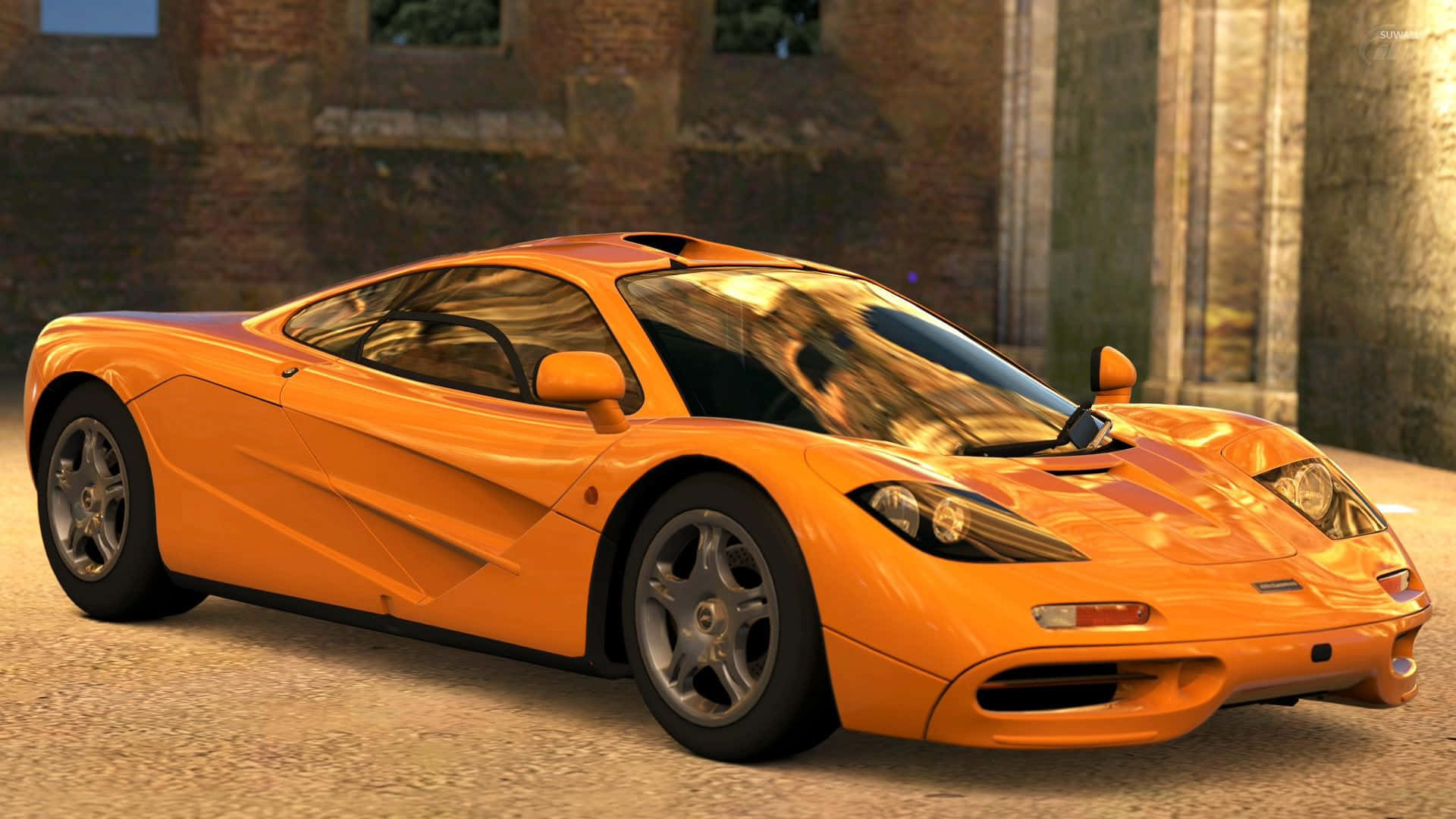 Mclaren F1 桌布 壁紙 — 一輛充滿活力的橙色McLaren F1跑車在溫暖的人造燈光下閃閃發光，背景是風化的磚砌建築。