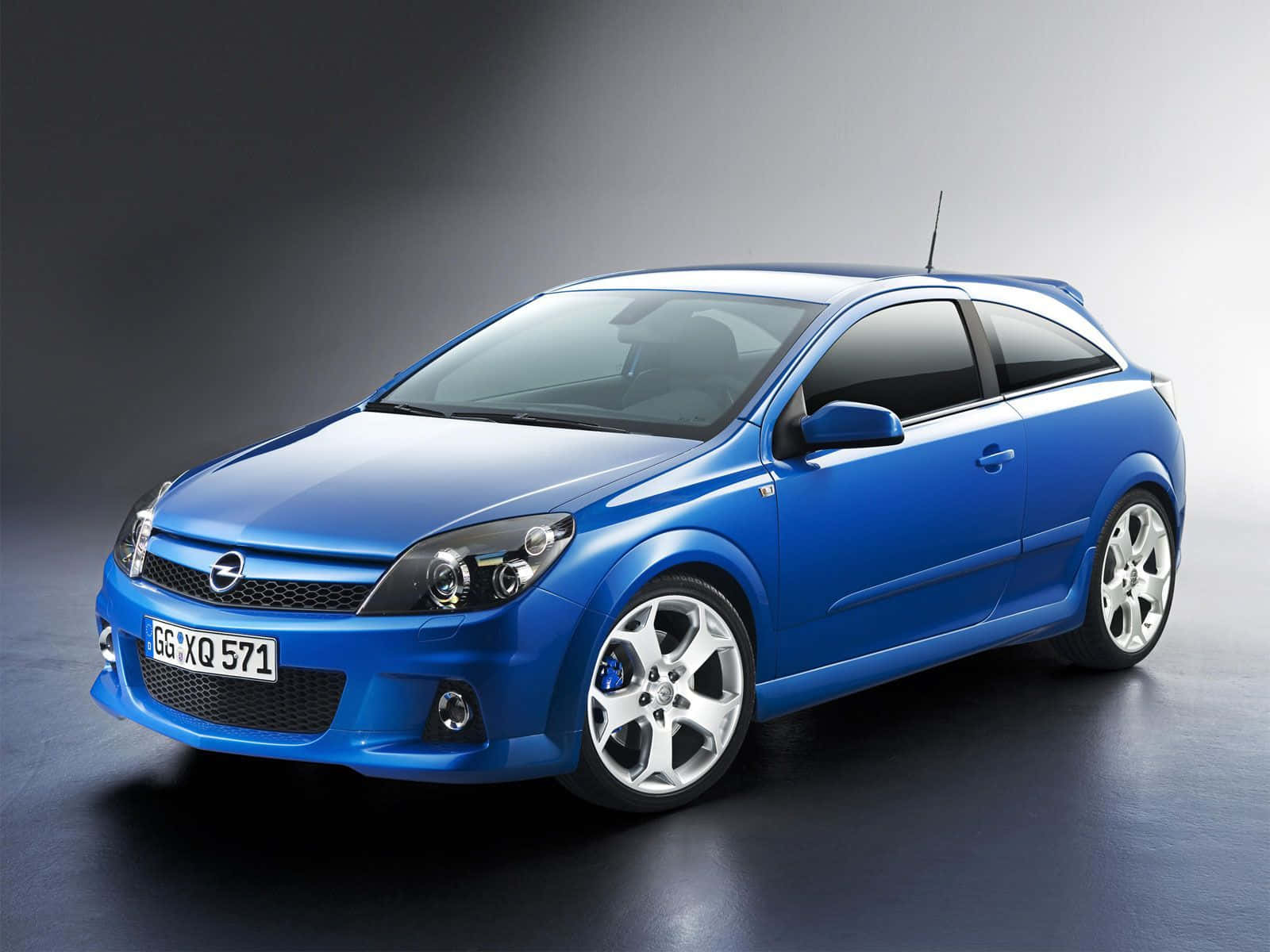 Opel Astra 桌布 壁紙 — 一輛充滿活力的藍色歐寶雅特GTC跑車在攝影棚燈光下閃閃發光，背景為深色漸變。