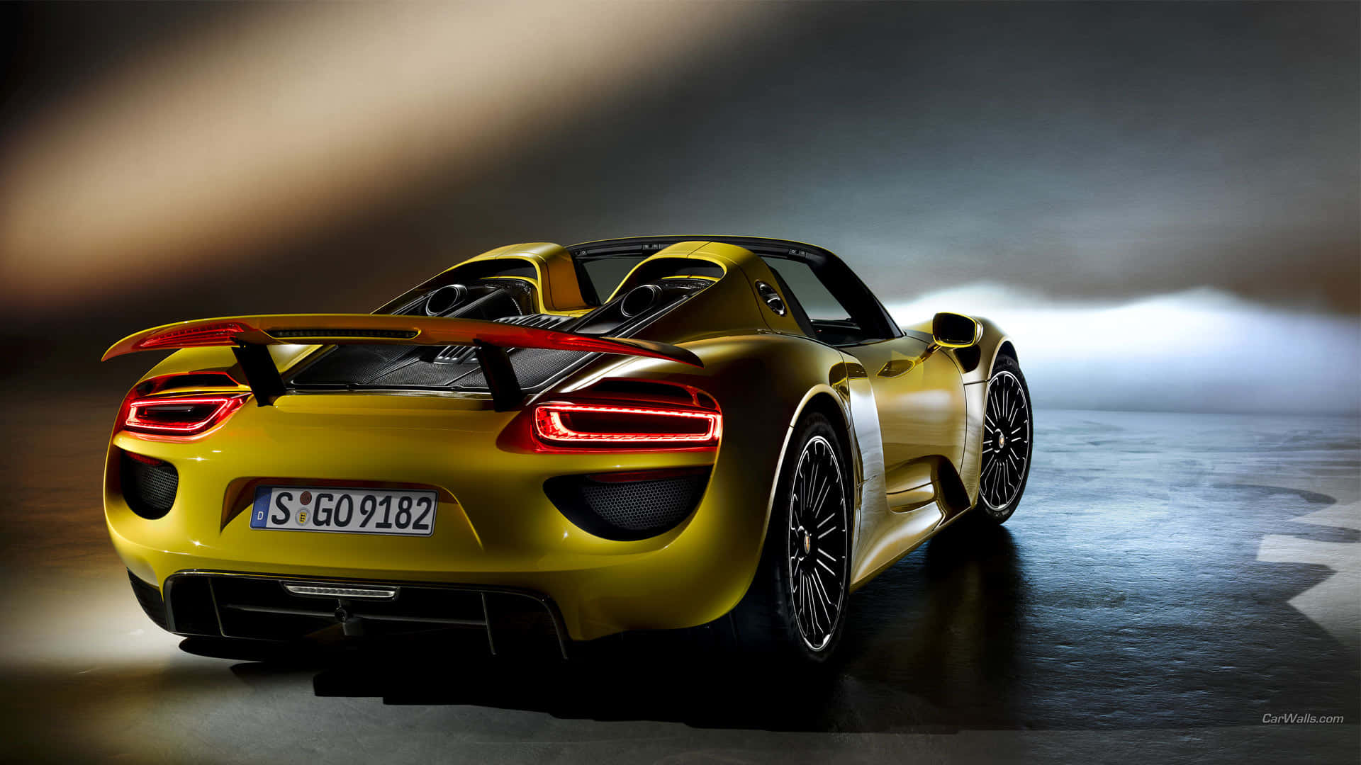 金色保時捷918 Spyder跑車，帶有紅色尾燈，在迷濛的工作室環境中。