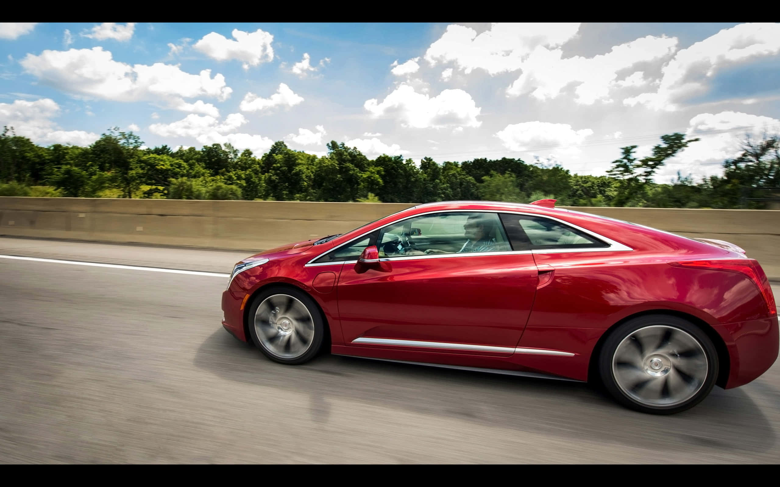 Cadillac Elr 桌布 壁紙 — 一輛鮮紅色的電動車在明亮的藍天白雲下高速行駛在高速公路上。