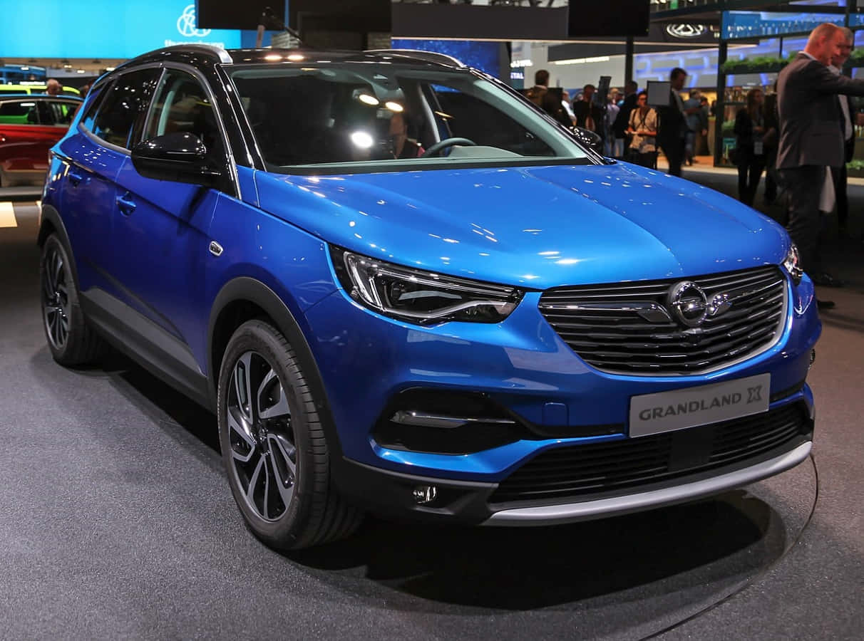 Opel Grandland X 桌布 壁紙 — 一輛鮮藍色的Opel Grandland X SUV在繁忙的車展上，在明亮的展覽燈光下閃閃發光。