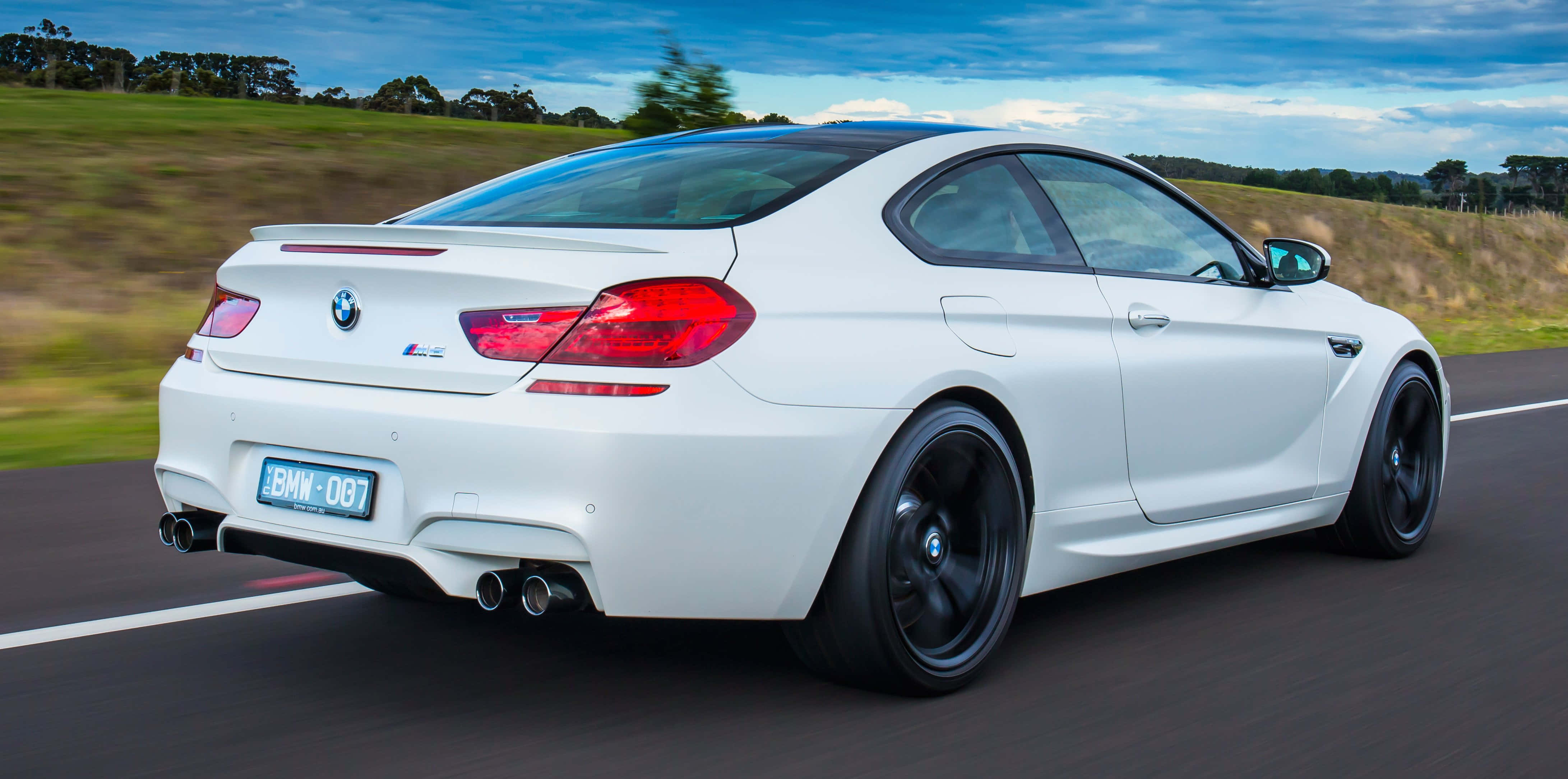 Bmw M6 桌布 壁紙 — 一輛白色BMW M6雙門跑車在鄉村道路上飛馳，背景是模糊的綠色田野和藍天。