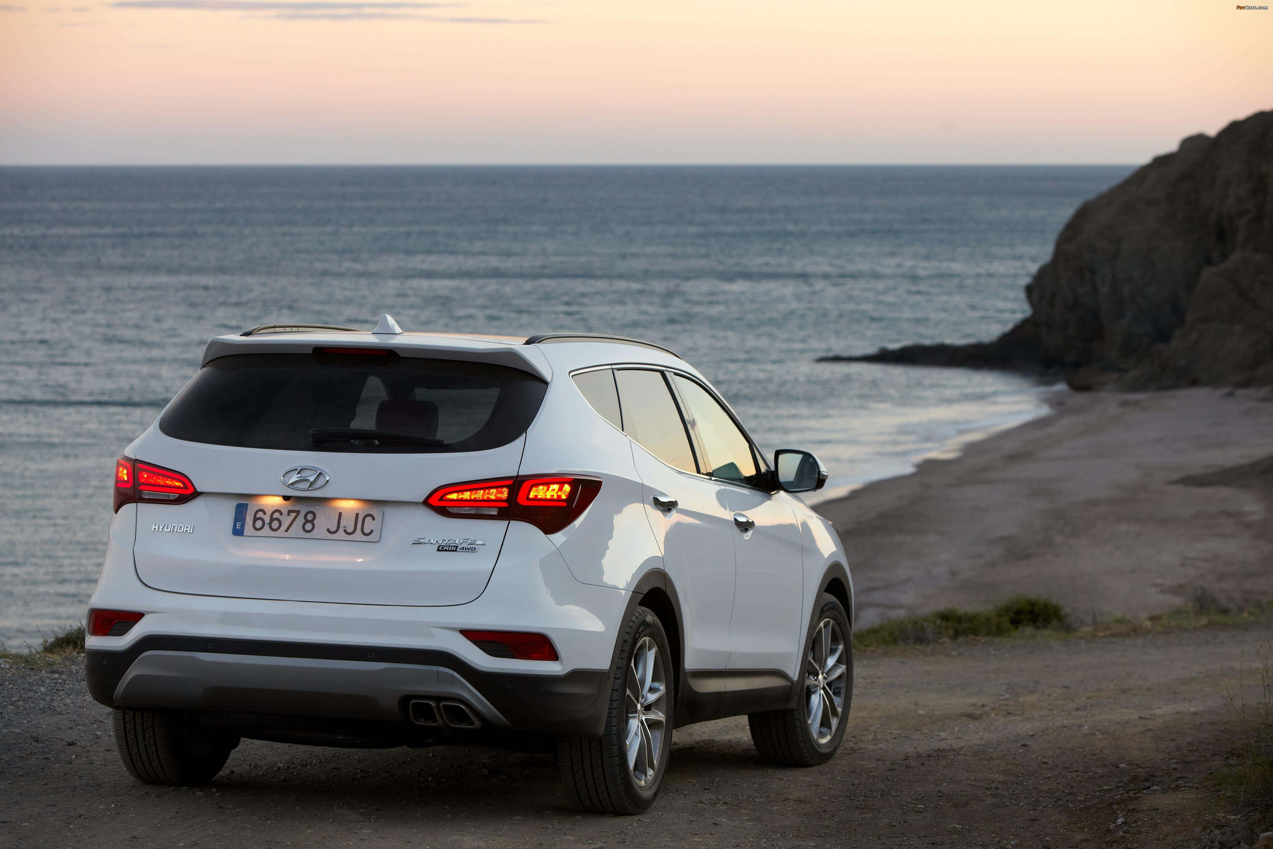 Hyundai Santa Fe 桌布 壁紙 — 一輛白色現代Santa Fe SUV在日落時分停泊在沿海泥路，背景有海洋和懸崖。