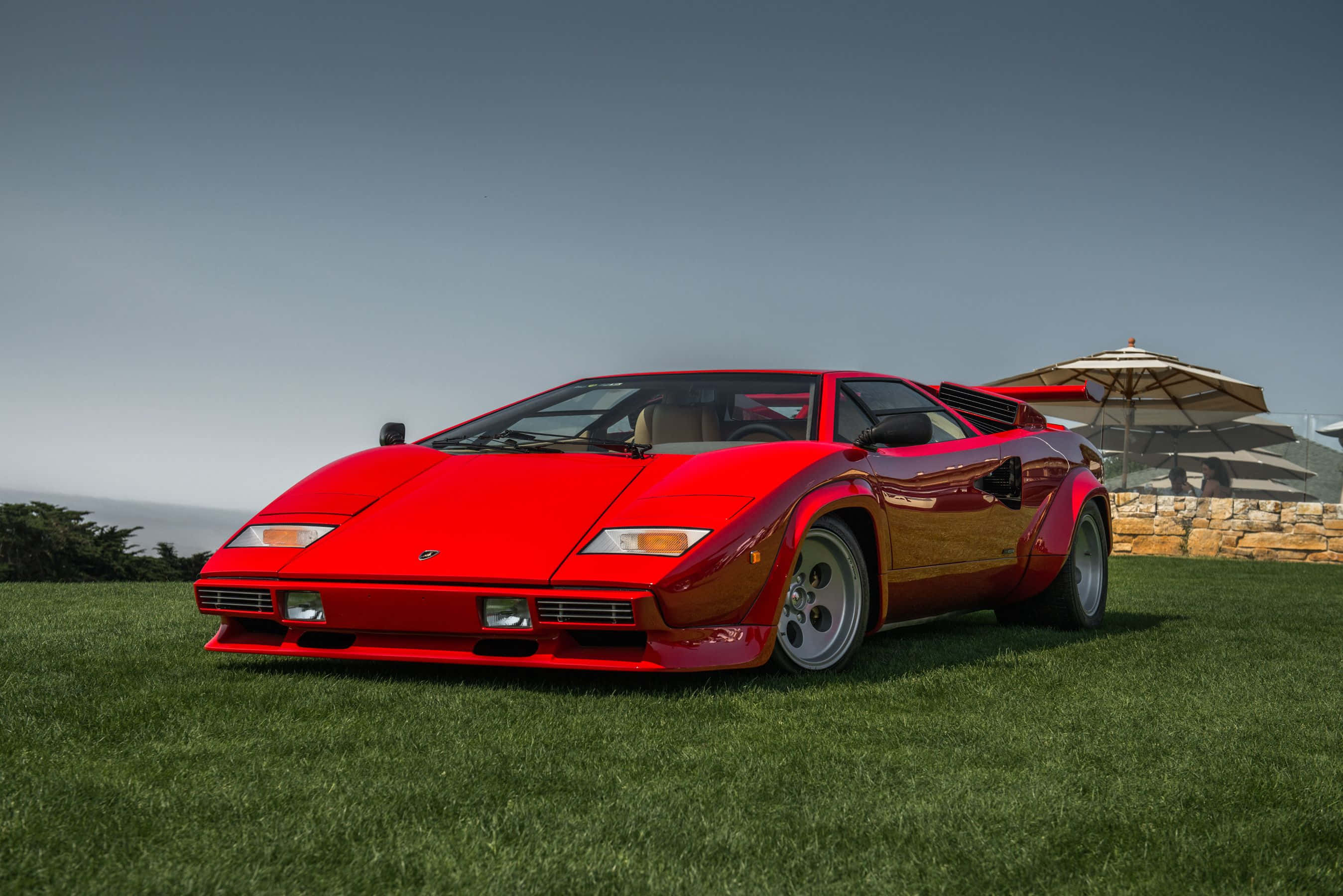 Lamborghini Countach 桌布 壁紙 — 一輛鮮紅色的林寶堅尼Countach停泊在茂盛的綠草地上，背景有海景和石牆。