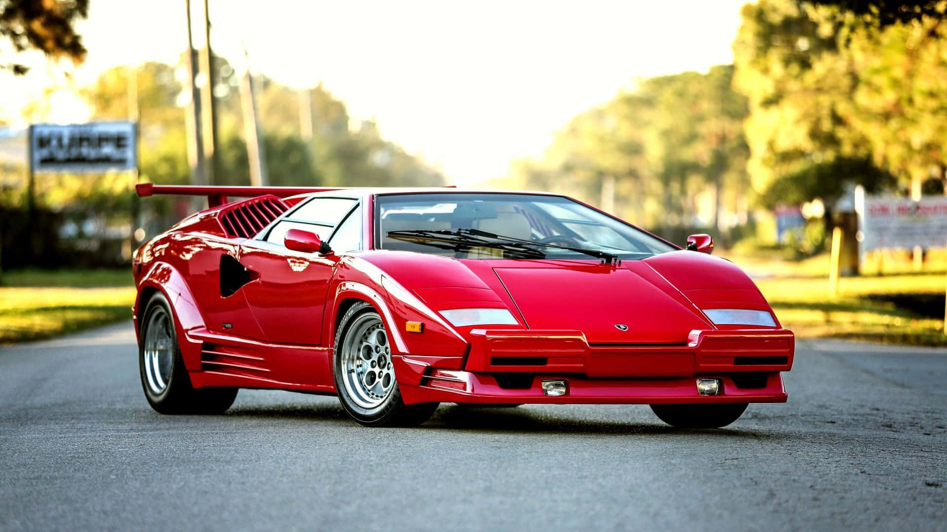 Lamborghini Countach 桌布 壁紙 — 一輛鮮紅色的林寶堅尼Countach停泊在陽光普照的道路上，背景有樹木和柔和的金色光線。