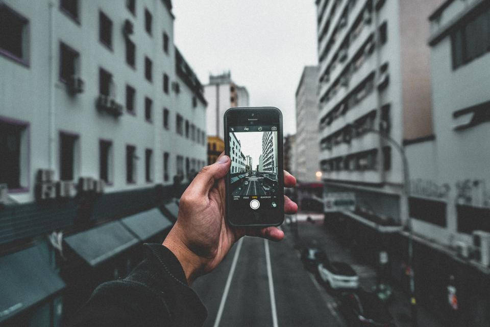 人拿著手機拍攝高樓之間的城市街道。