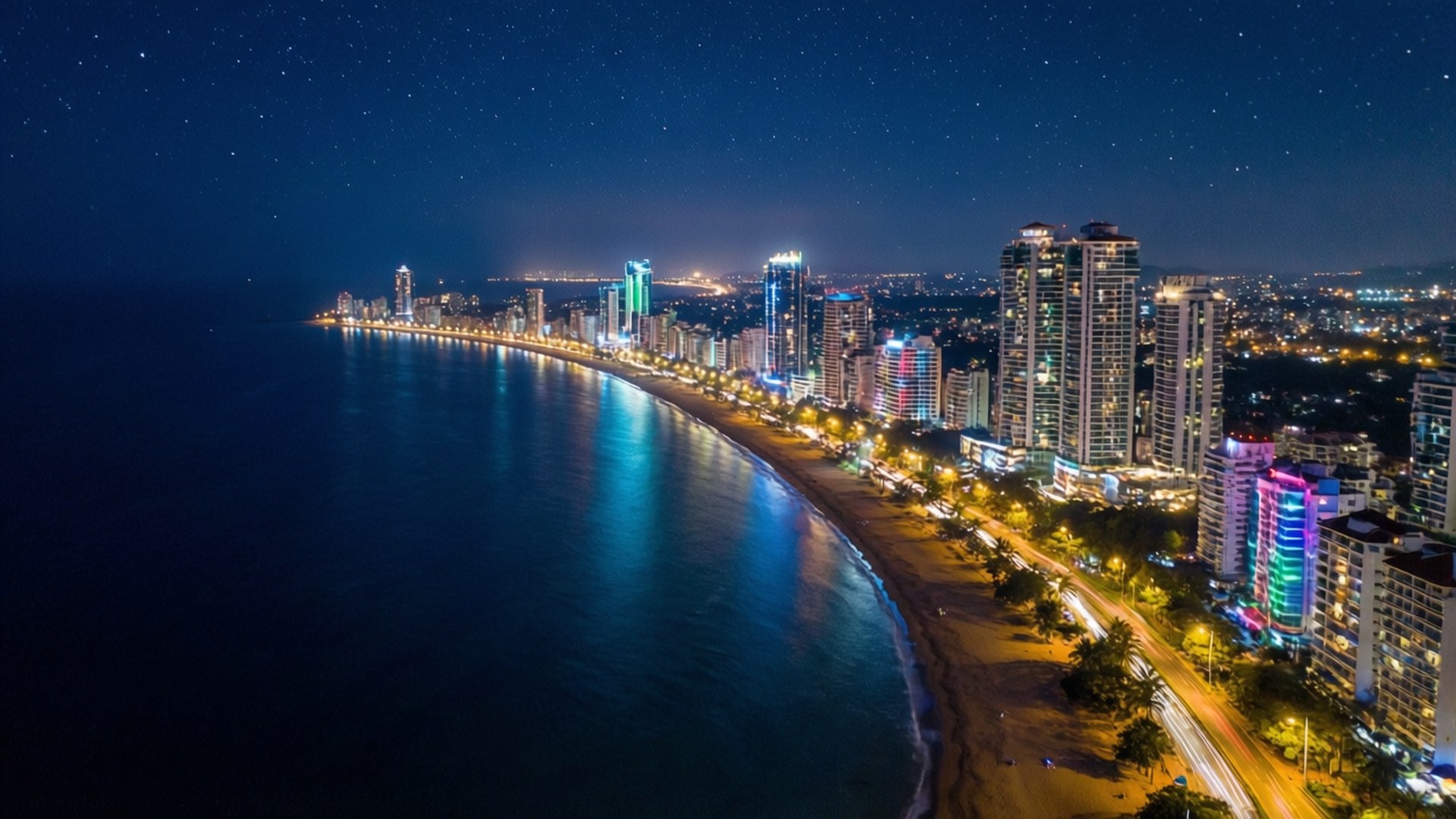Mumbai 桌布 壁紙 — 在深藍色海水下，閃爍的摩天大樓、星空和燈火通明的海濱構成的迷人夜間沿海城市景觀。