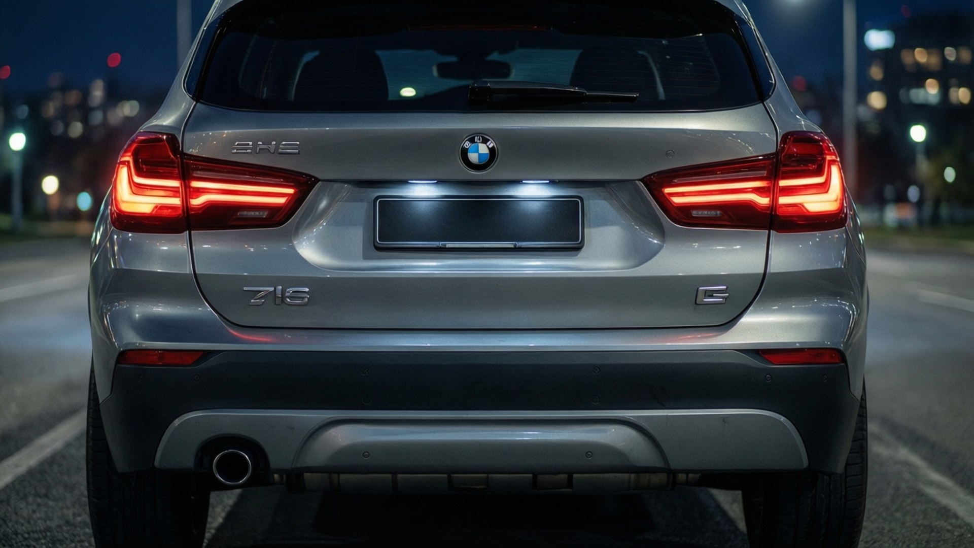 Bmw X1 桌布 壁紙 — 夜晚中，一輛銀色寶馬X5 SUV的後視圖，紅色尾燈在模糊的城市景觀中發光。