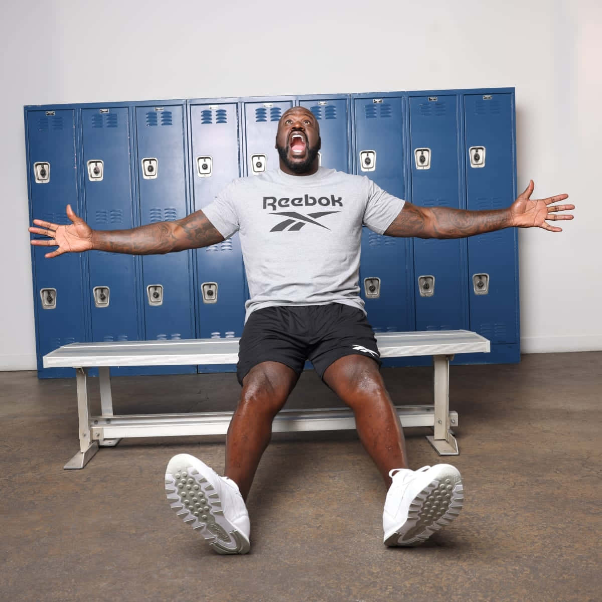  壁紙 — 一個穿著Reebok衫嘅肌肉男坐在 locker room 嘅長凳上，張開雙臂大叫。