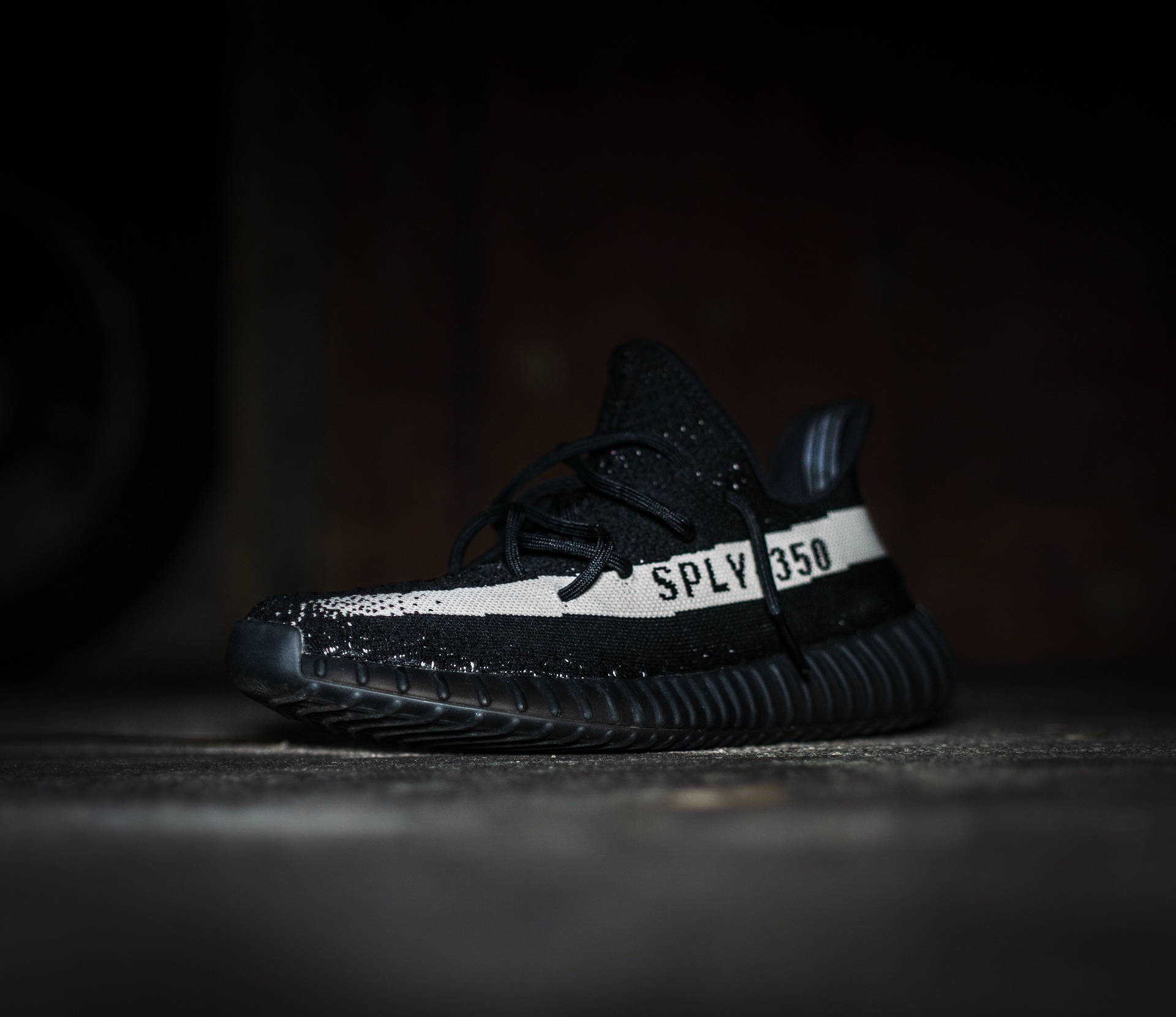 黑色Yeezy Boost 350運動鞋，在深色混凝土上帶有白色條紋
