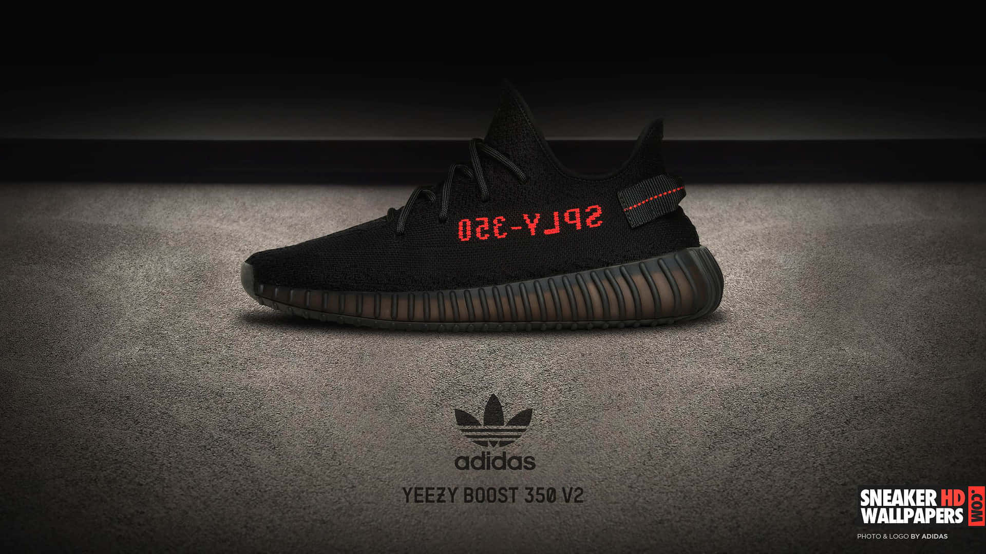 黑色Yeezy Boost 350 V2運動鞋，灰色紋理背景上帶有紅色文字。
