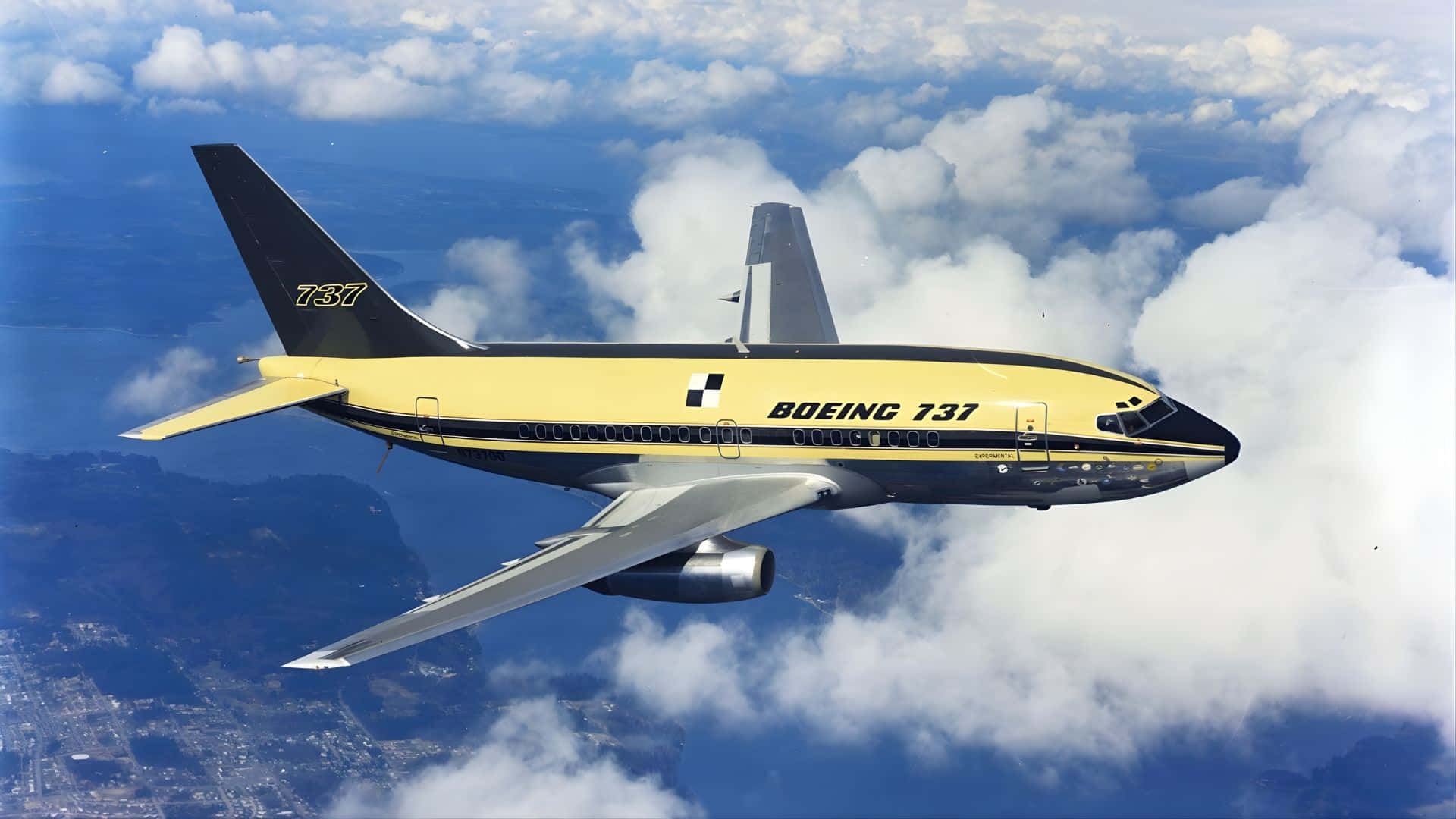  壁紙 — 一架黃黑相間的波音737飛機在藍天和遠方風景下的蓬鬆白雲上方翱翔。