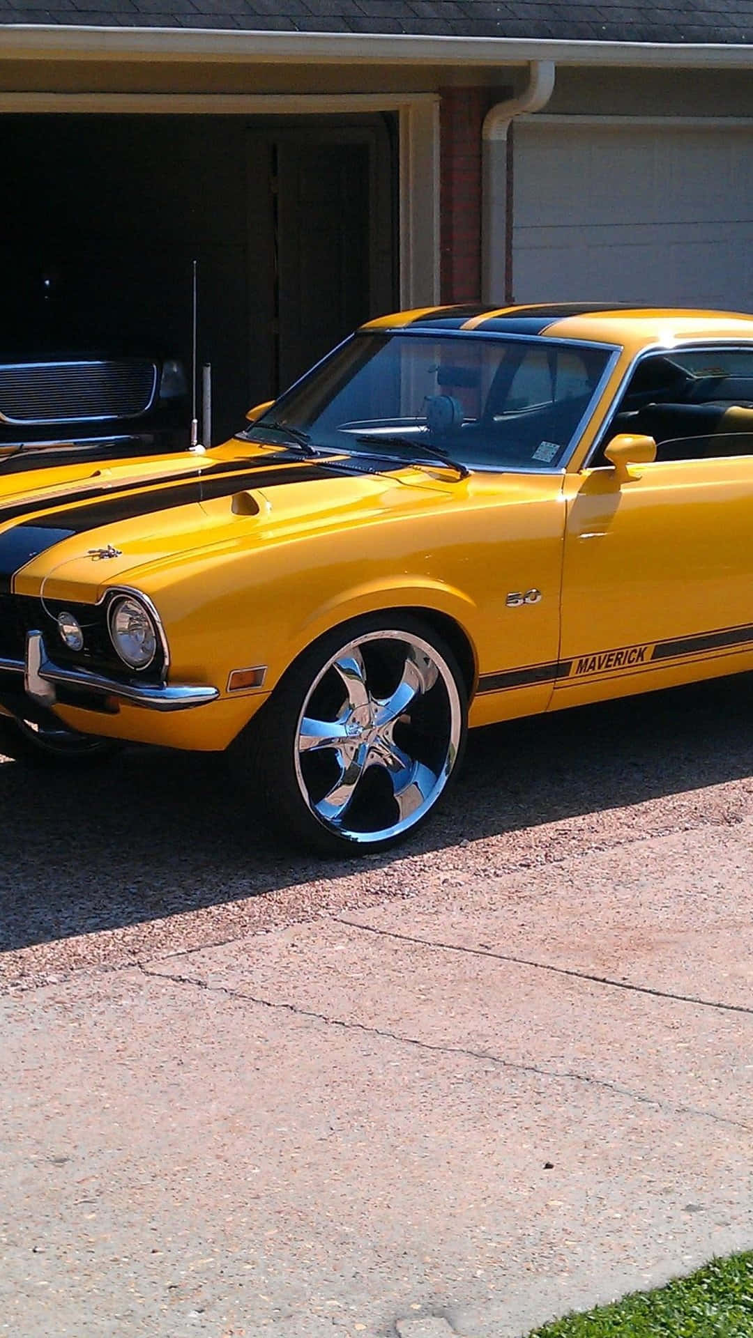 Ford Maverick 桌布 壁紙 — 一輛亮黃色經典肌肉車，帶有黑色賽車條紋，停在車庫前的混凝土車道上。