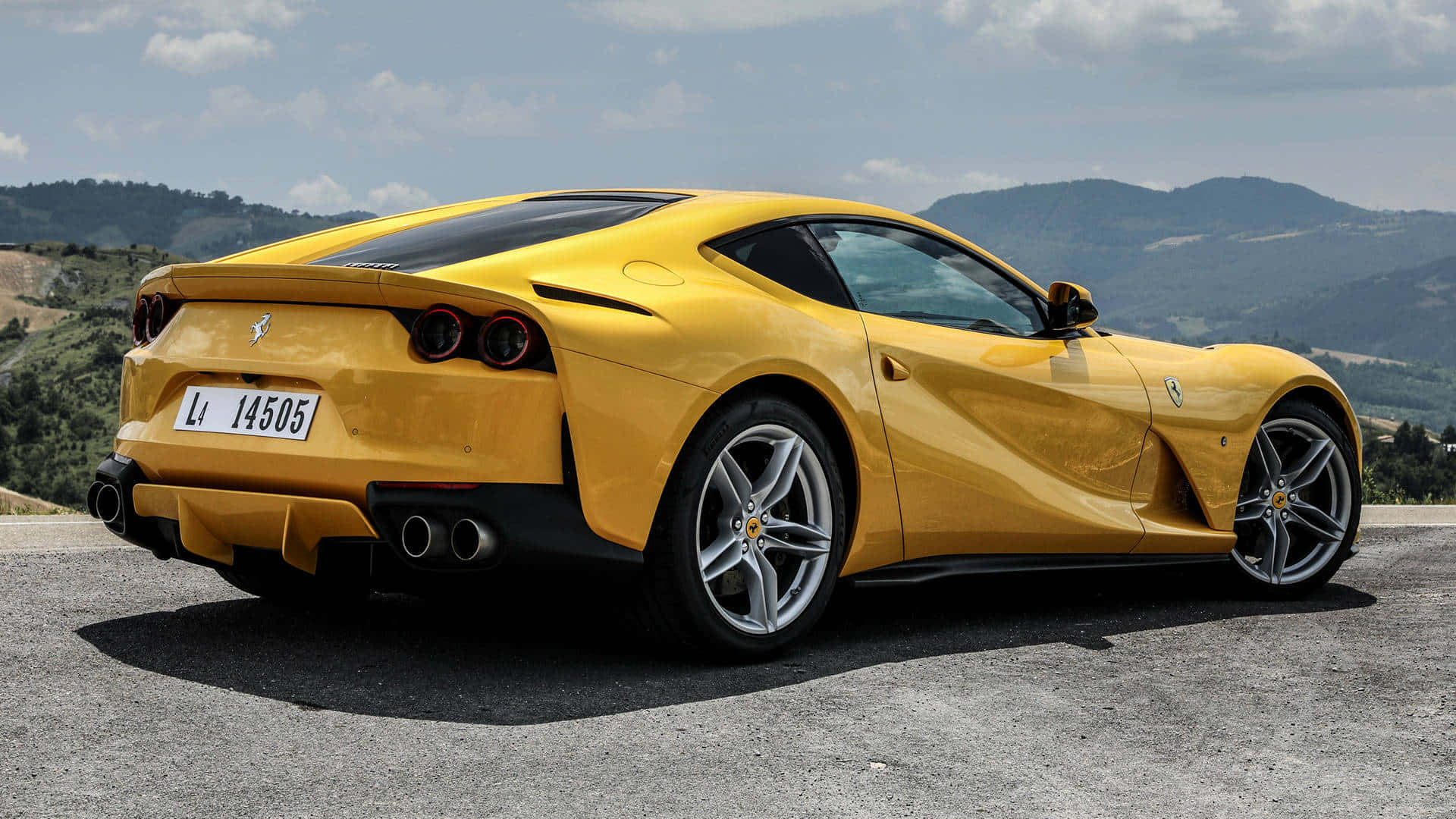 Ferrari 812 Superfast 桌布 壁紙 — 一輛鮮黃色的法拉利跑車停泊在山路上，背景是起伏的山丘和多雲的天空。