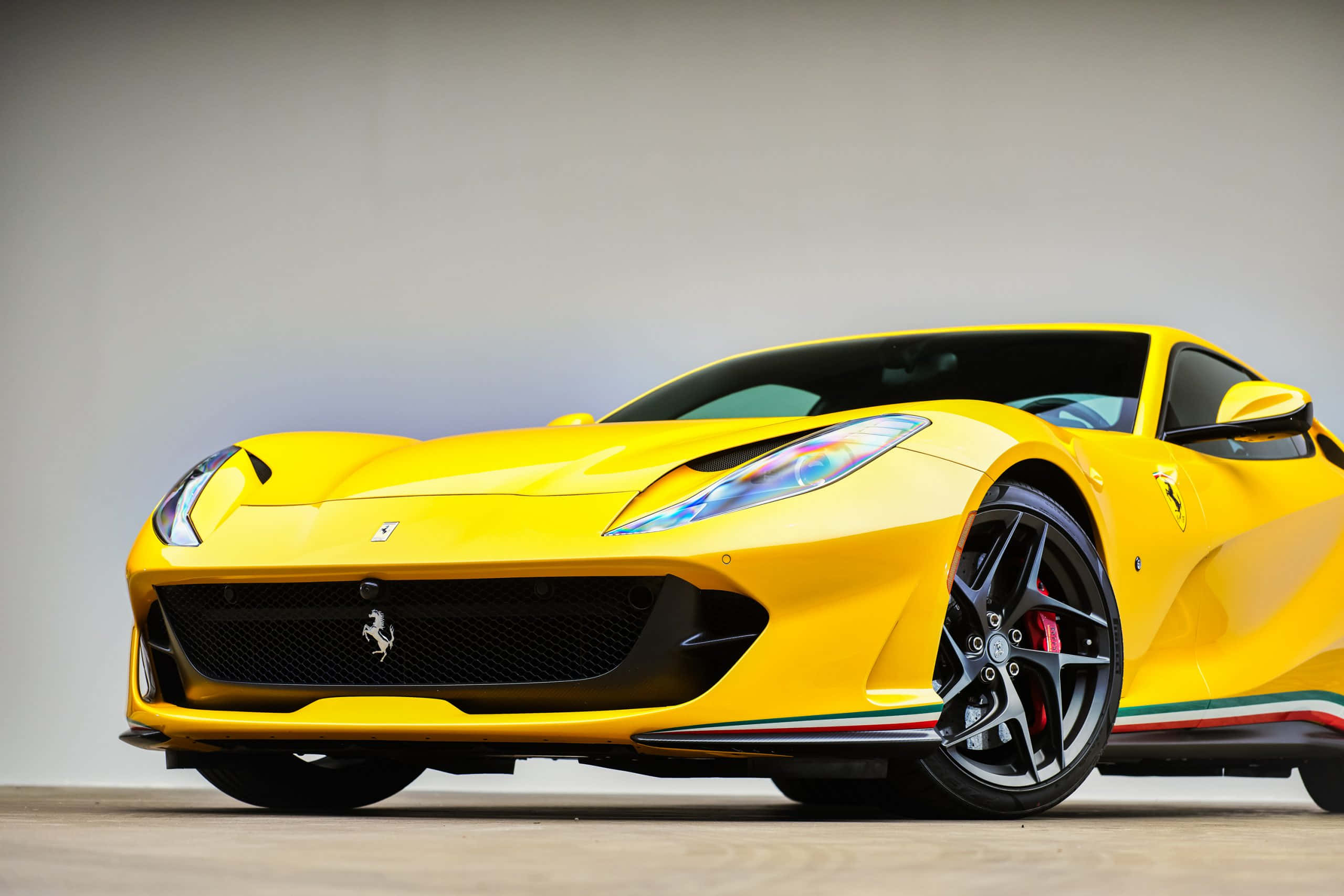 Ferrari 812 Superfast 桌布 壁紙 — 一輛充滿活力的黃色法拉利跑車，帶有黑色飾件和紅色制動卡鉗，在中性攝影棚背景下擺拍。