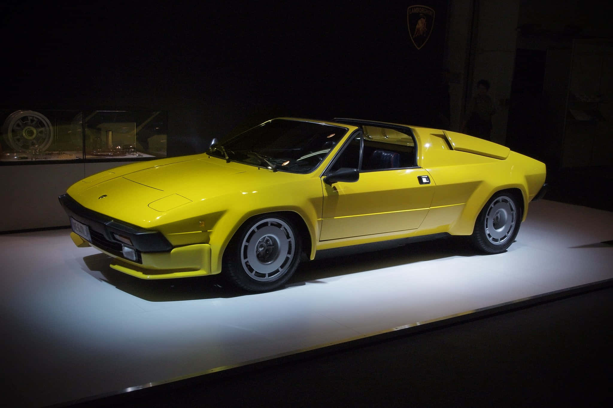 Lamborghini Silhouette 桌布 壁紙 — 一輛鮮黃色的林寶堅尼Countach跑車在黑暗的博物館環境中，於白色展示台上在聚光燈下閃閃發光。