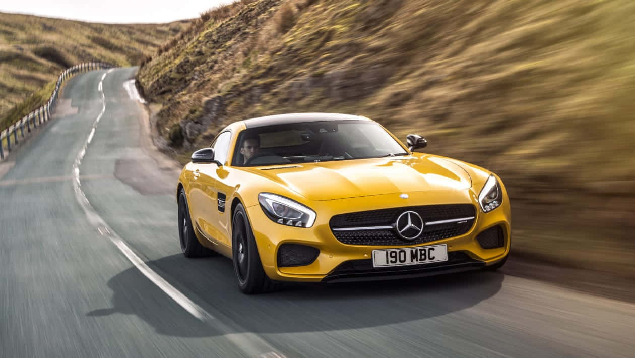 Mercedes Benz Amg Gt 桌布 壁紙 — 一輛鮮黃色的 Mercedes-AMG GT S 在蜿蜒的山路上疾馳，兩旁是模糊的草地山坡。