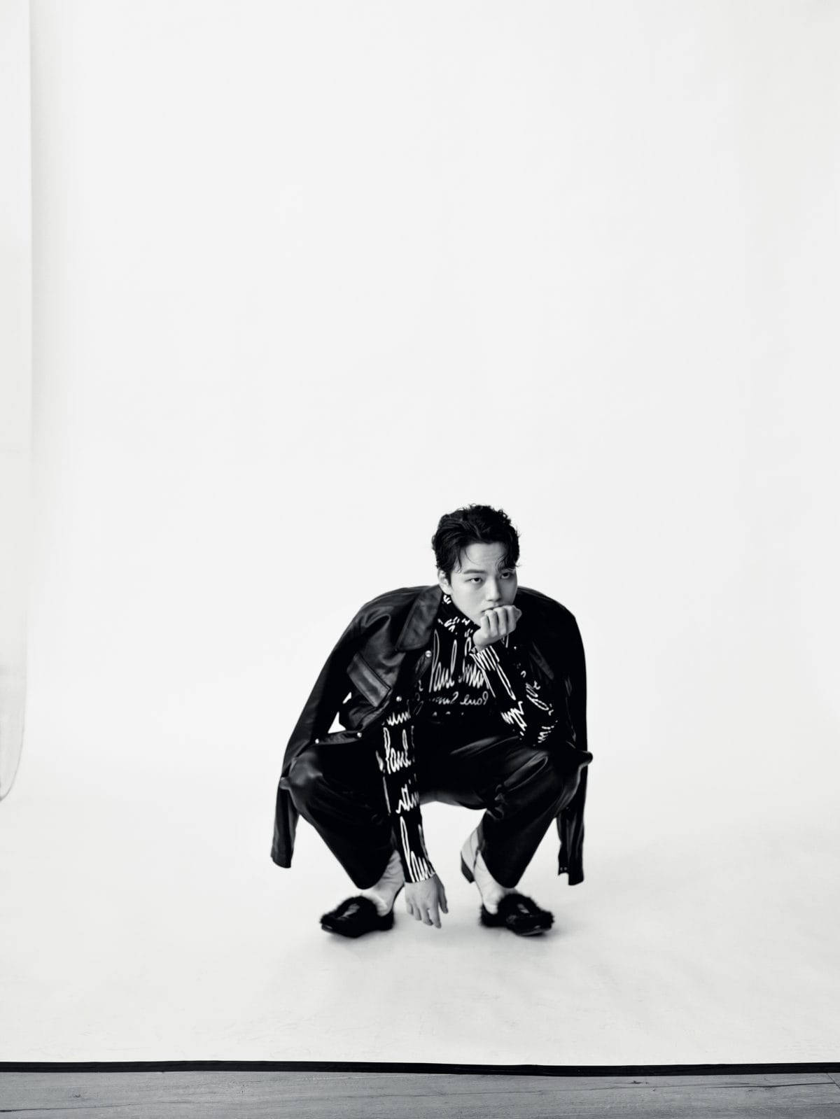 Yeo Jin Goo 穿黑色皮夾克，智性時尚 壁紙 — 一名身穿黑色皮革服裝的男子，在單色調的純白工作室背景前若有所思地蹲下。