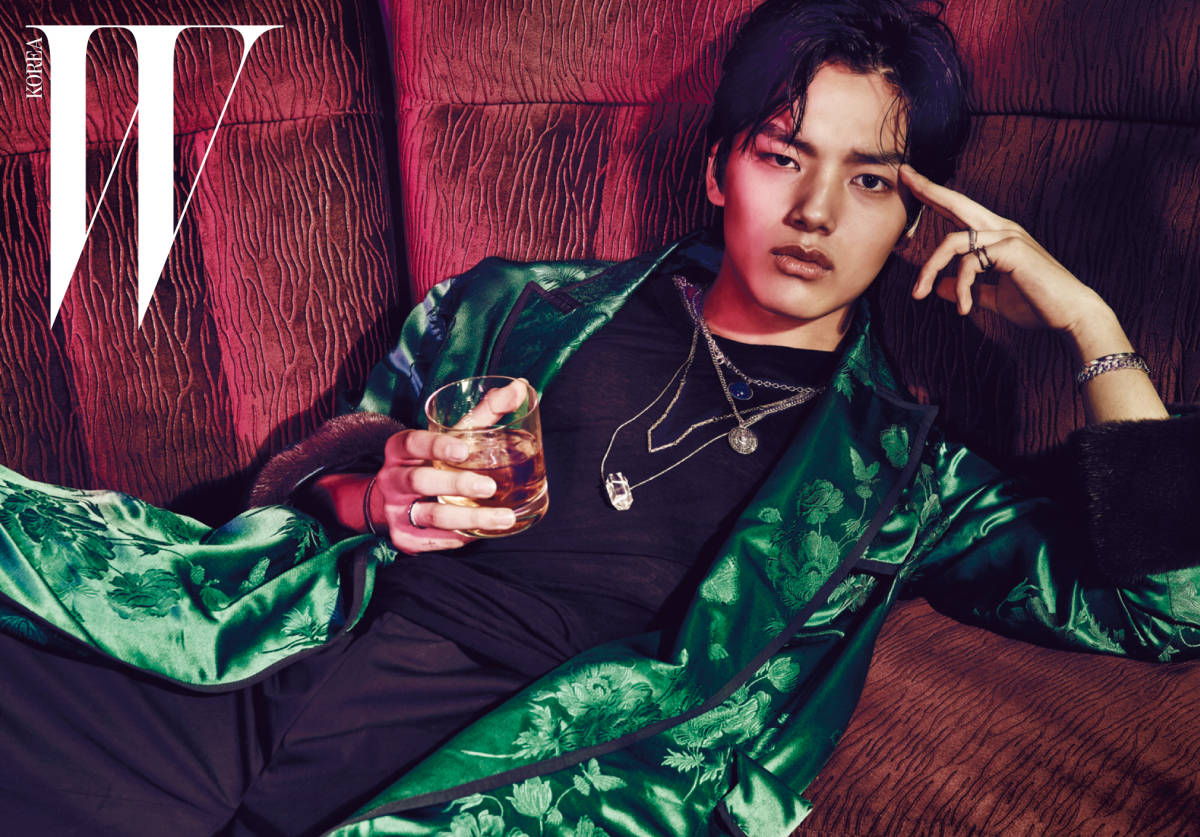 Yeo Jin Goo 為《W》雜誌拍攝 壁紙 — 一位時尚年輕男子身穿綠色花卉緞面長袍，手持一杯威士忌，慵懶地躺在紅色紋理沙發上。
