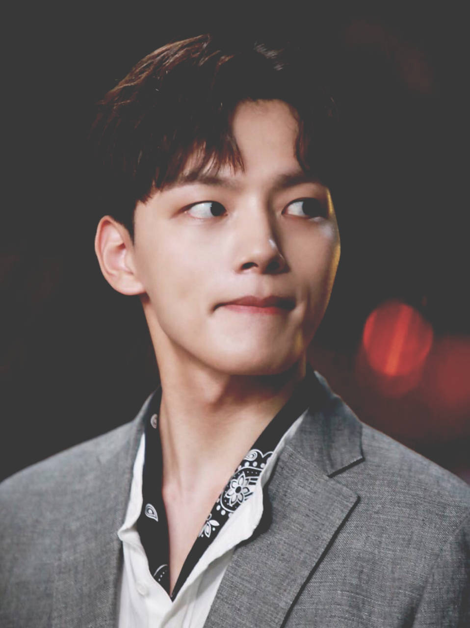 Yeo Jin Goo 穿灰色禮服 壁紙 — 一位身穿灰色西裝和圖案襯衫的年輕男子，在帶有溫暖散景燈光的黑暗背景下，側目而視，帶著微妙的微笑。